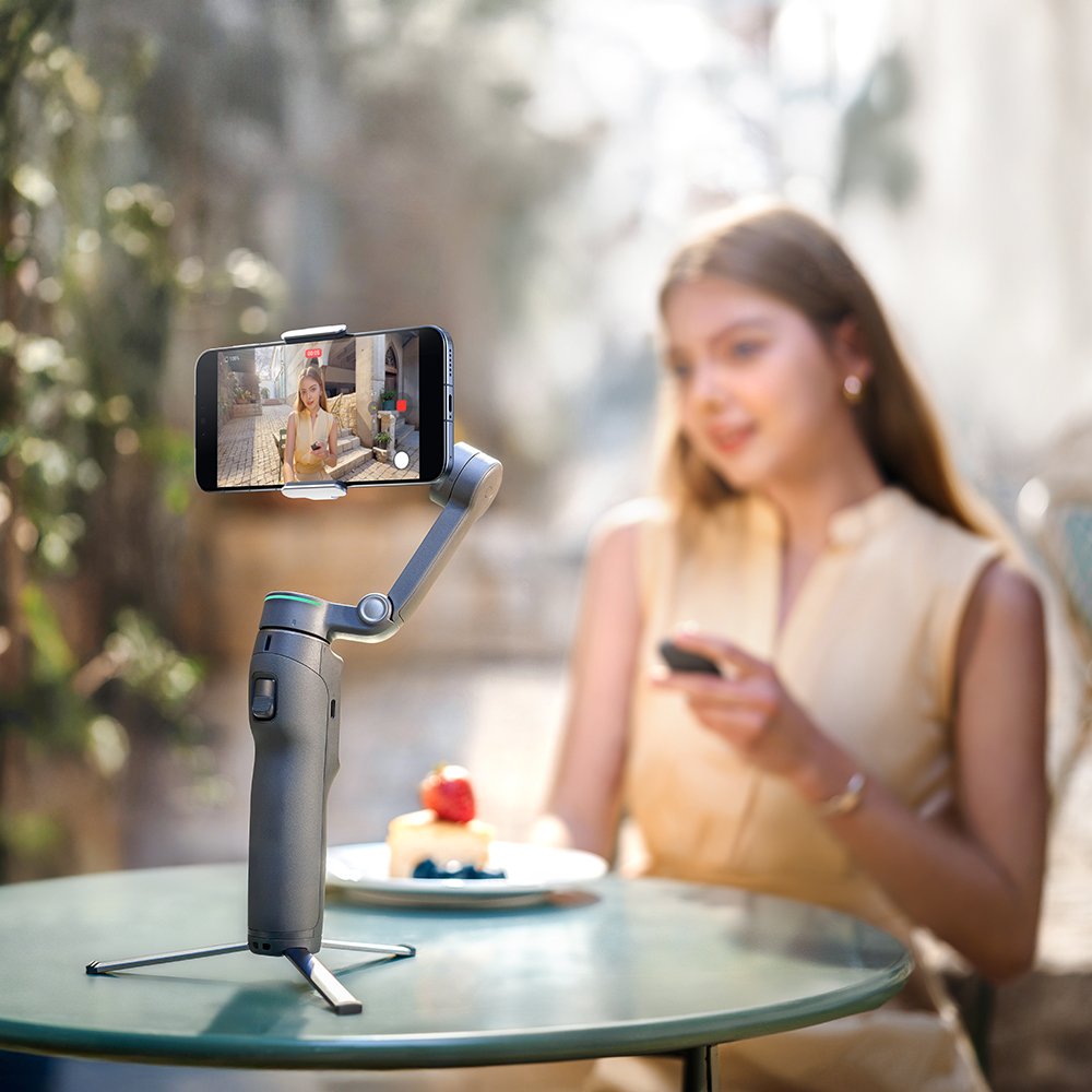 Bir gimbal, bir kadını gösteren akıllı telefonu tutuyor. Masada bir pasta var.