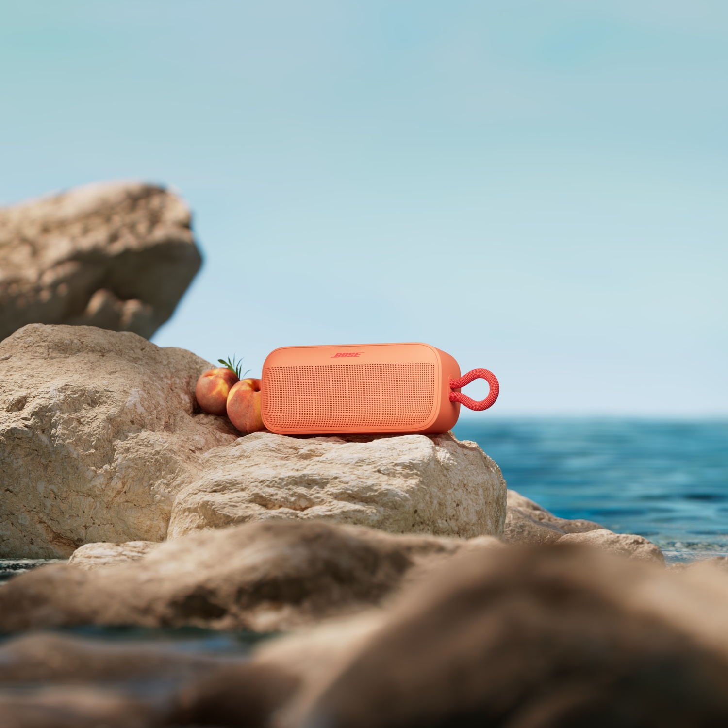 Een oranje Bose speaker op rotsen aan zee, met perziken ernaast.