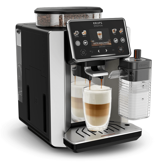 Eine schwarze Krups-Kaffeemaschine bereitet einen Latte Macchiato in einem klaren Glas zu.