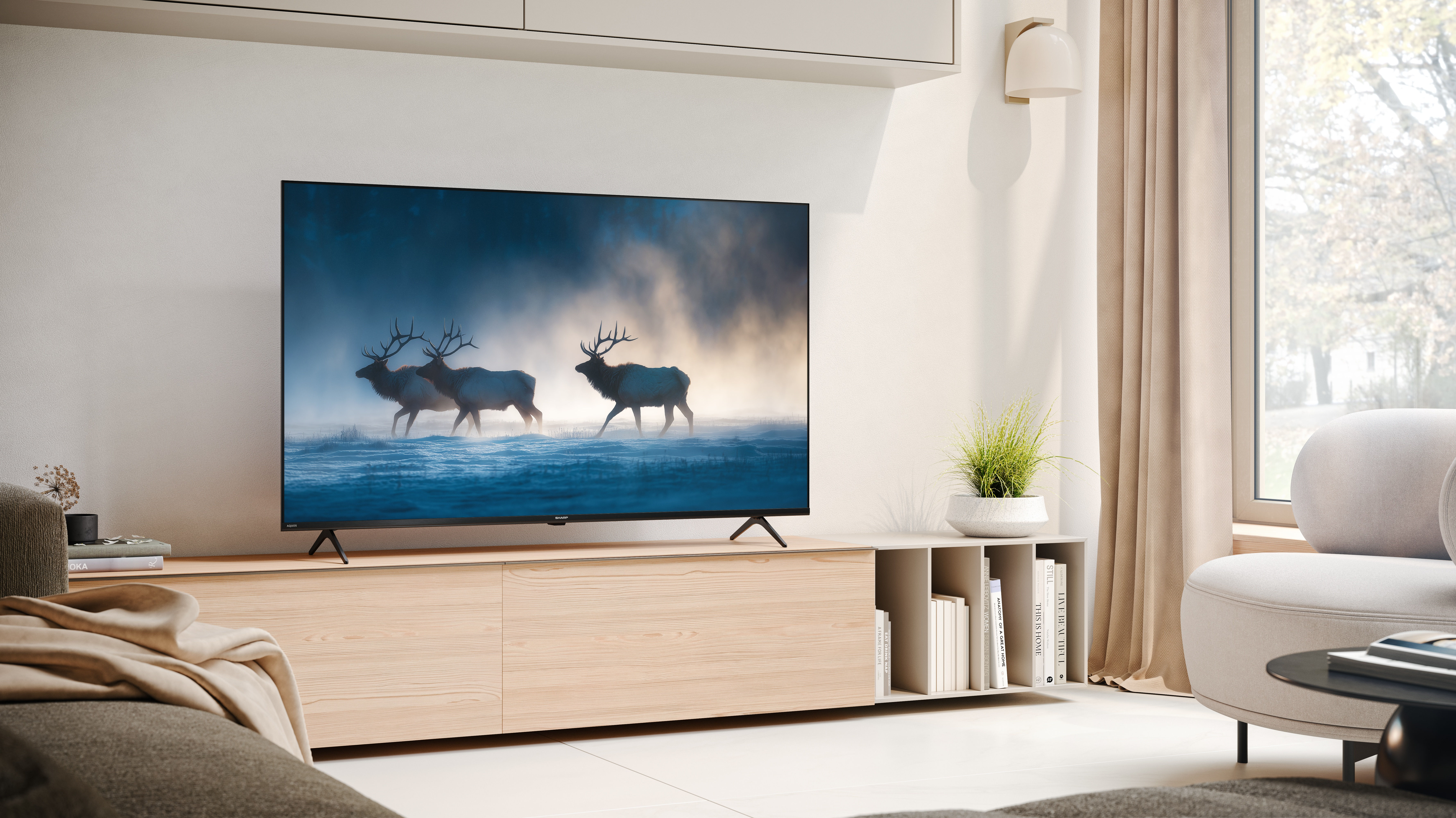 Telewizor pokazuje jelenie na śniegu. Salon z sofą i oknem.