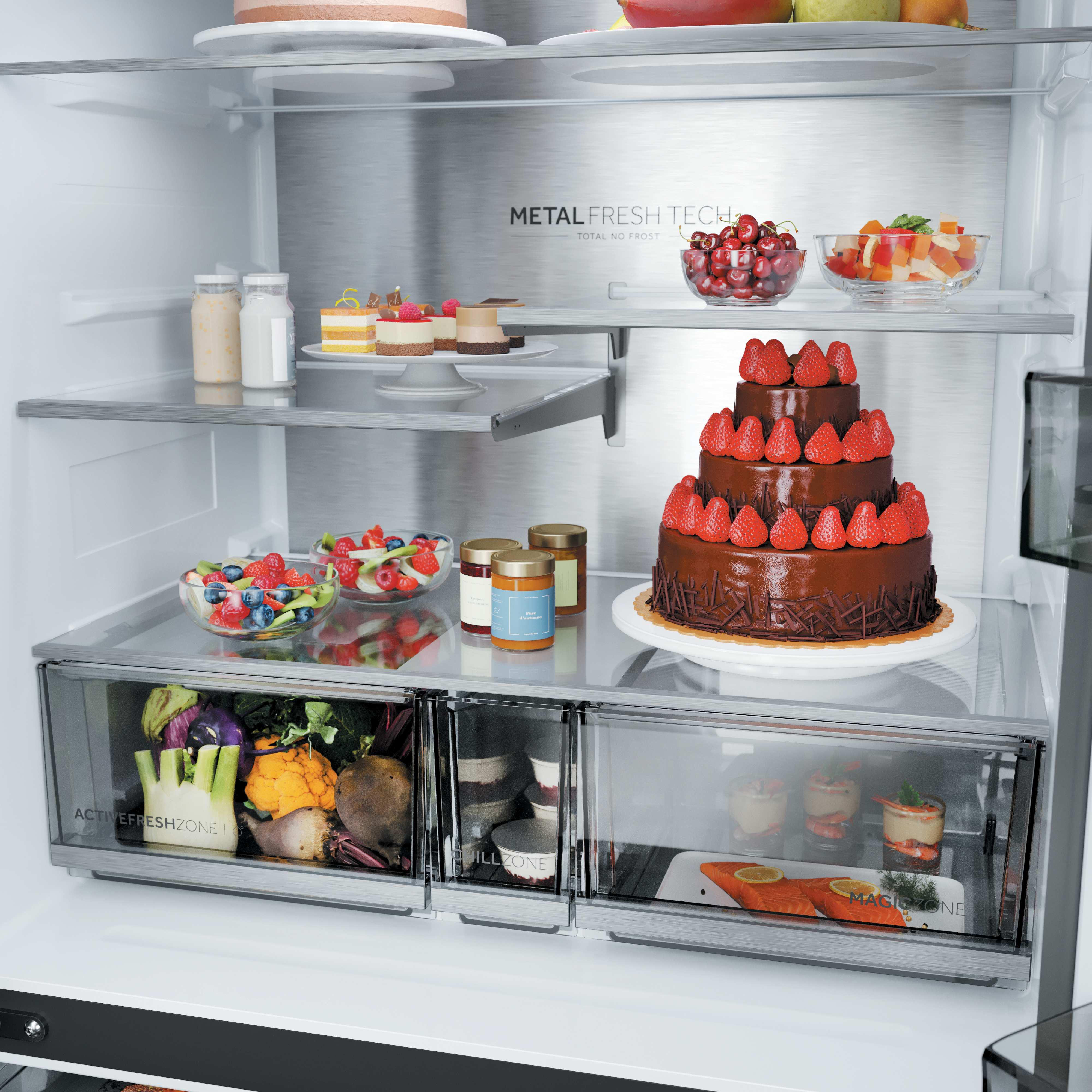 Ein Kühlschrank mit einem Schokoladenkuchen, Obstschalen, Desserts und Gemüse.