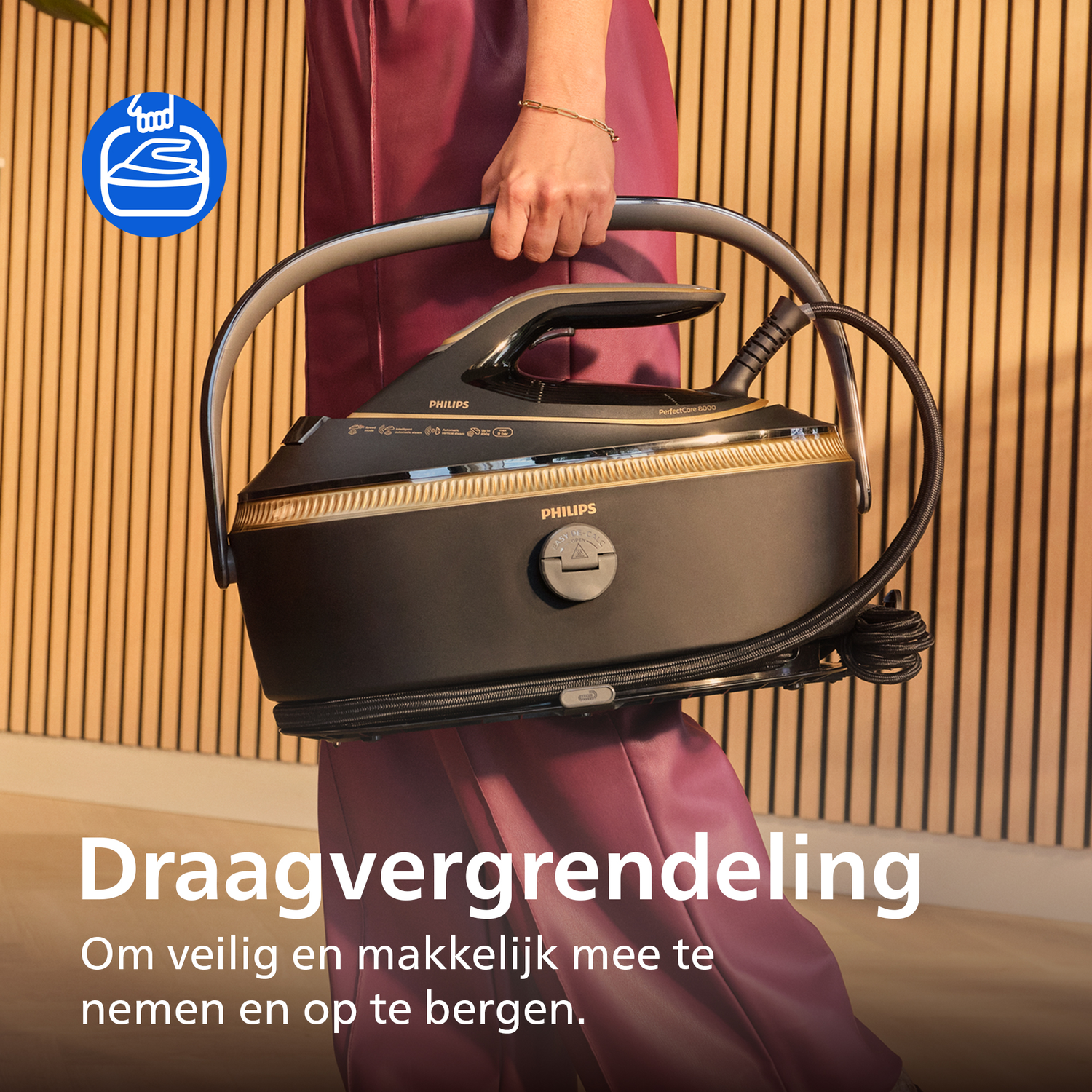 Een persoon houdt een zwart stoomstrijkijzer met zilveren handvat vast tegen een houten achtergrond.