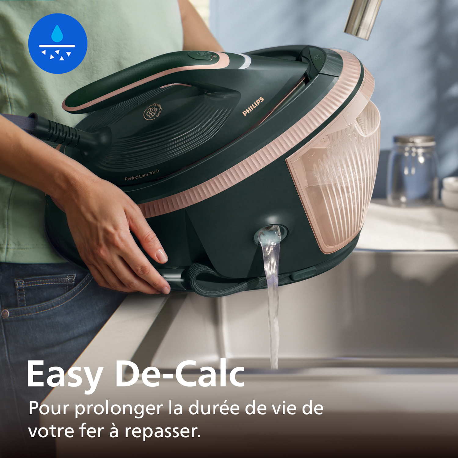 Une personne vide de l'eau d'un fer Philips vert foncé dans un évier. L'eau coule.