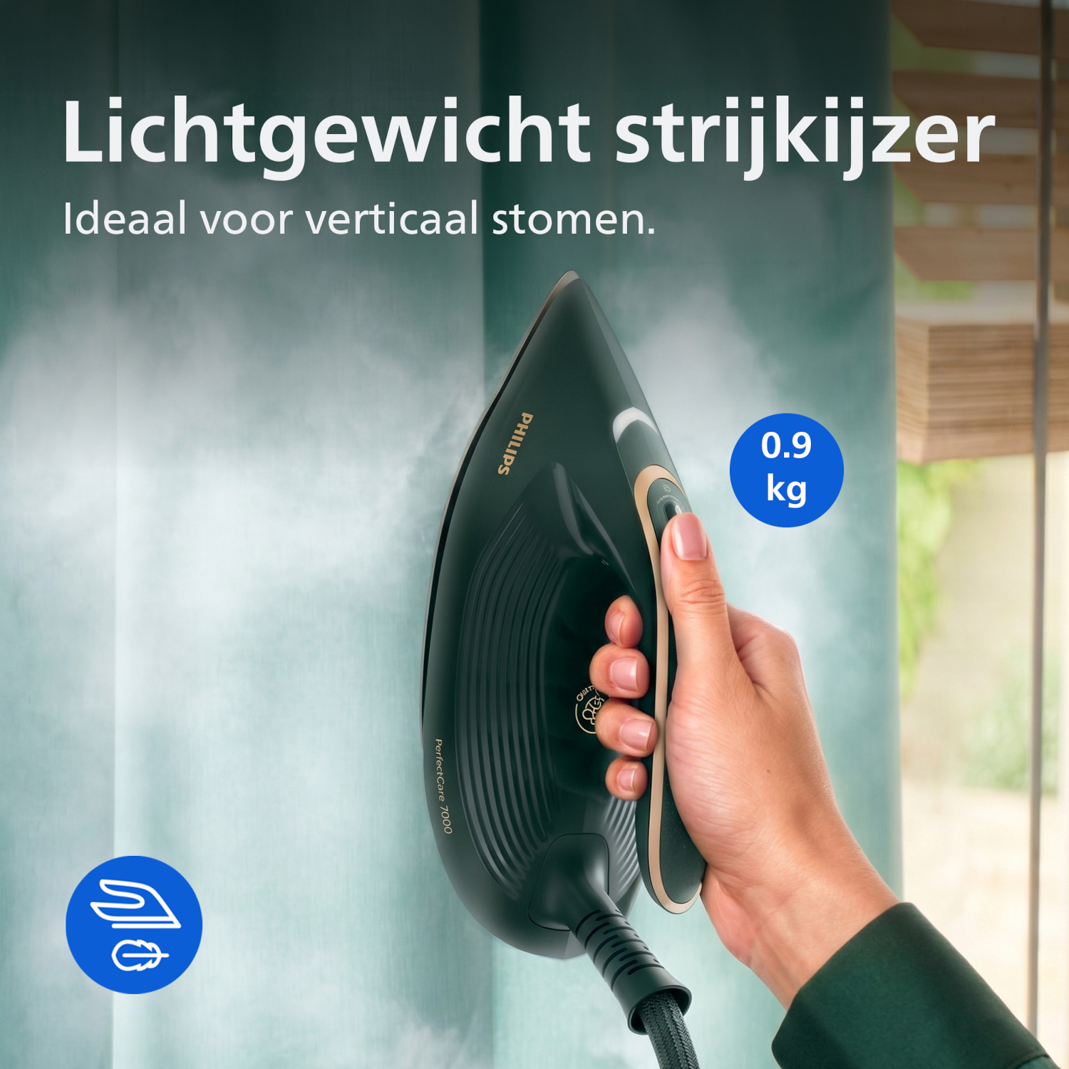 A hand holds a dark green steam iron smoothing fabric. 0.9 kg.