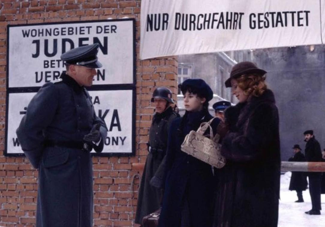 Ein Mann in Uniform steht vor Schildern. Frauen warten.