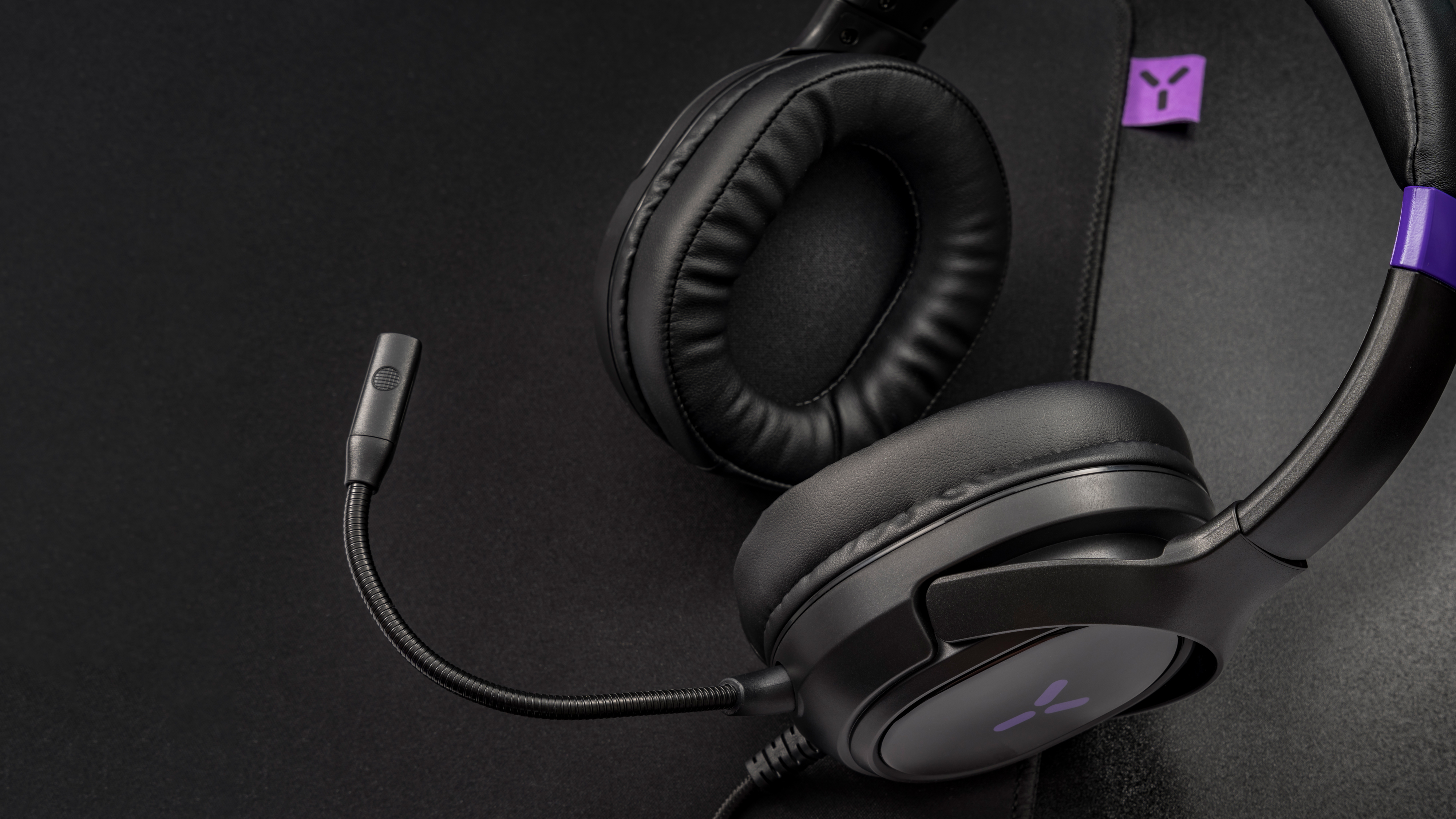 Black headphones with a microphone and purple logo on a black background.