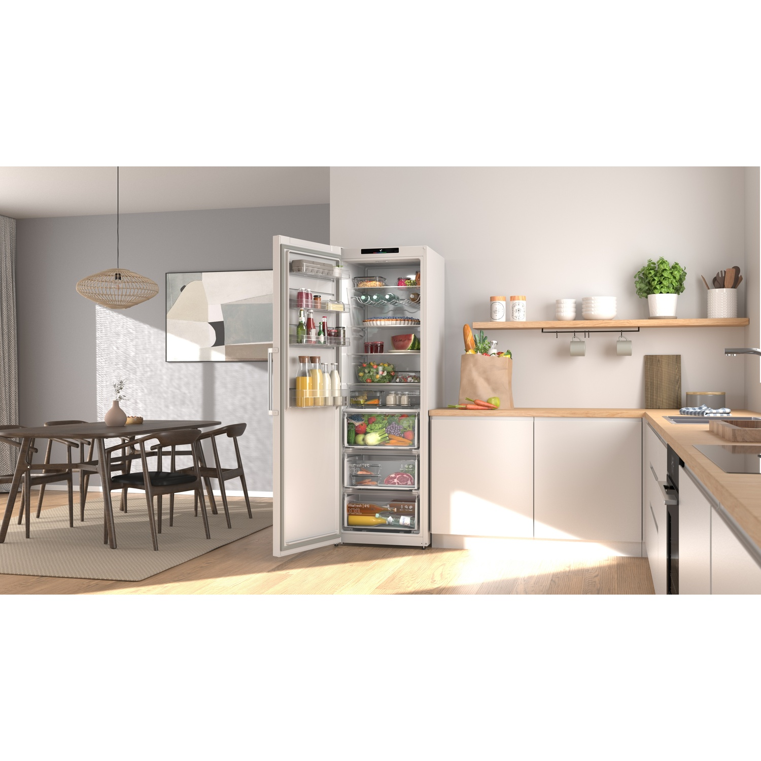 Réfrigérateur ouvert rempli de nourriture, à côté d'une table à manger dans une cuisine lumineuse.