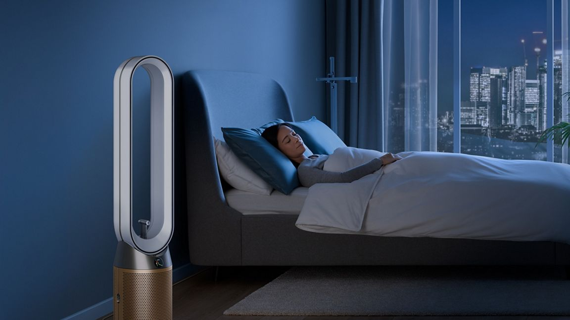 Femme dort au lit, purificateur d'air à côté, vue de ville la nuit derrière.