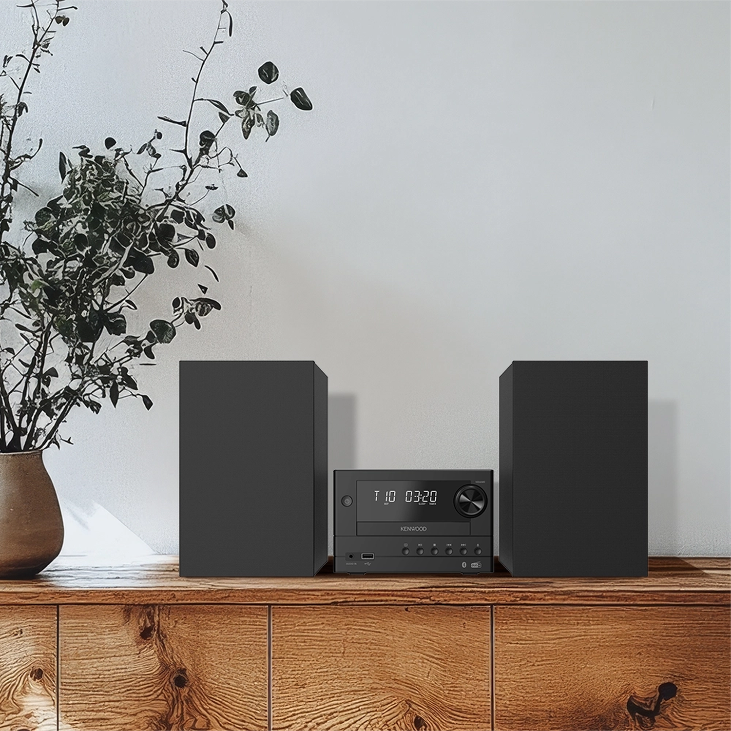 Schwarzes Kenwood-Stereo mit zwei Lautsprechern auf Holzregal. Pflanze in Vase links.