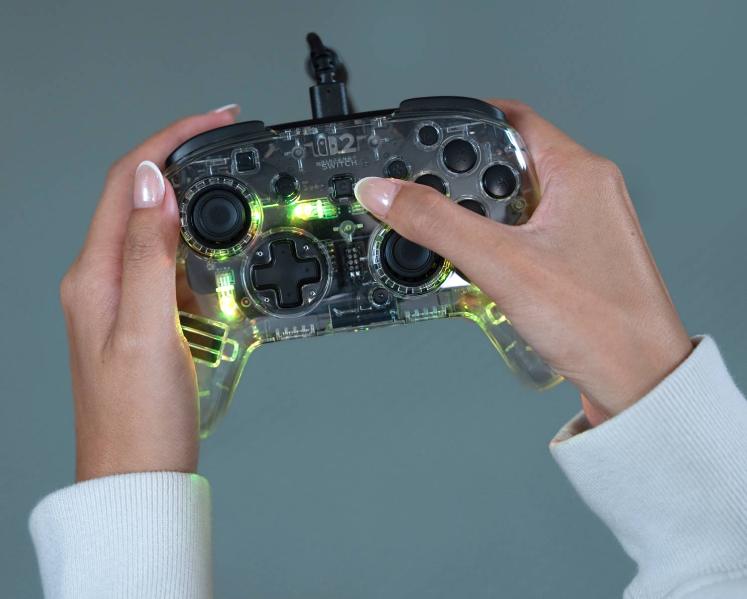 Persona sosteniendo controlador transparente con luces verdes, primer plano.