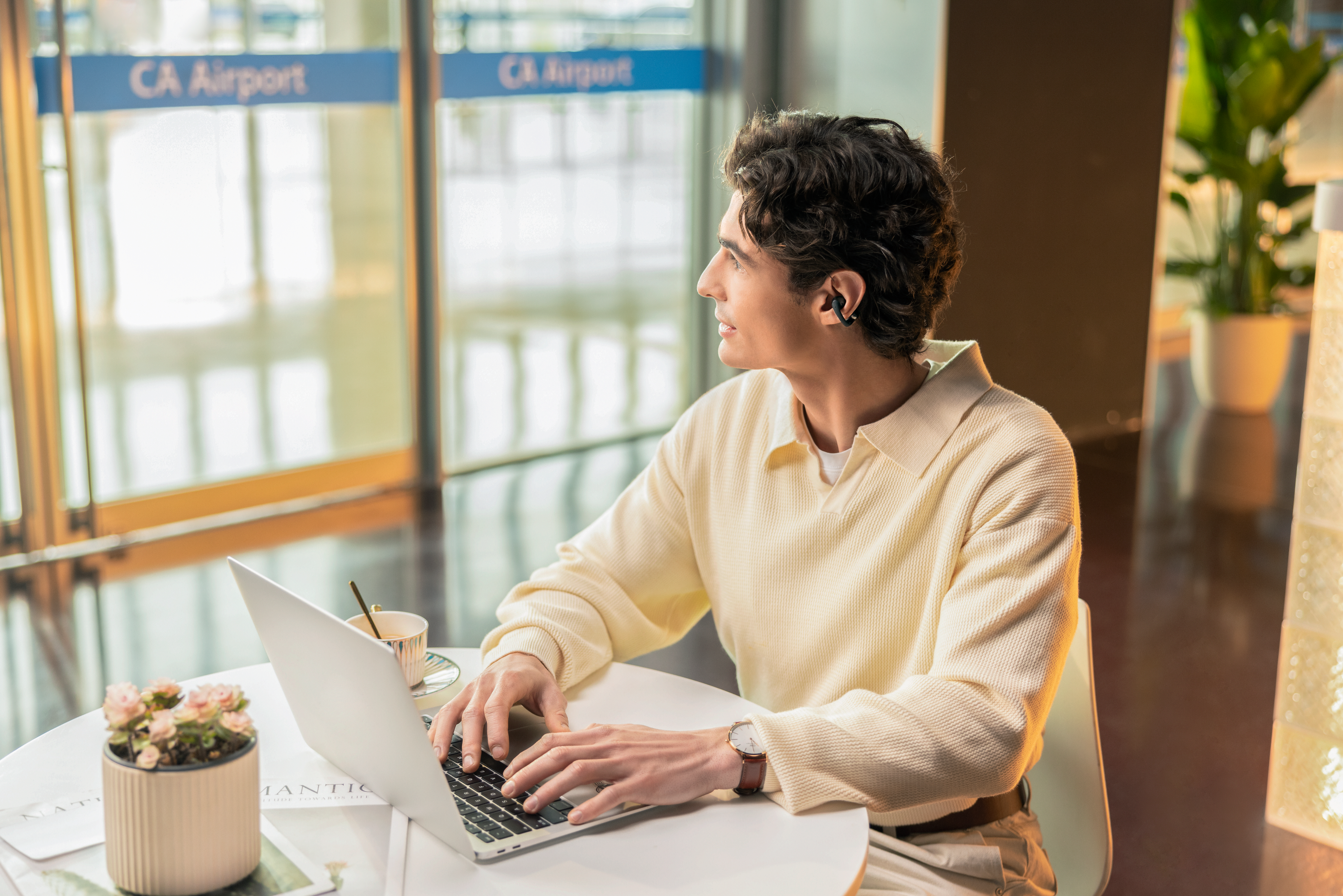 Un uomo con auricolari digita su un laptop in un bar dell'aeroporto.
