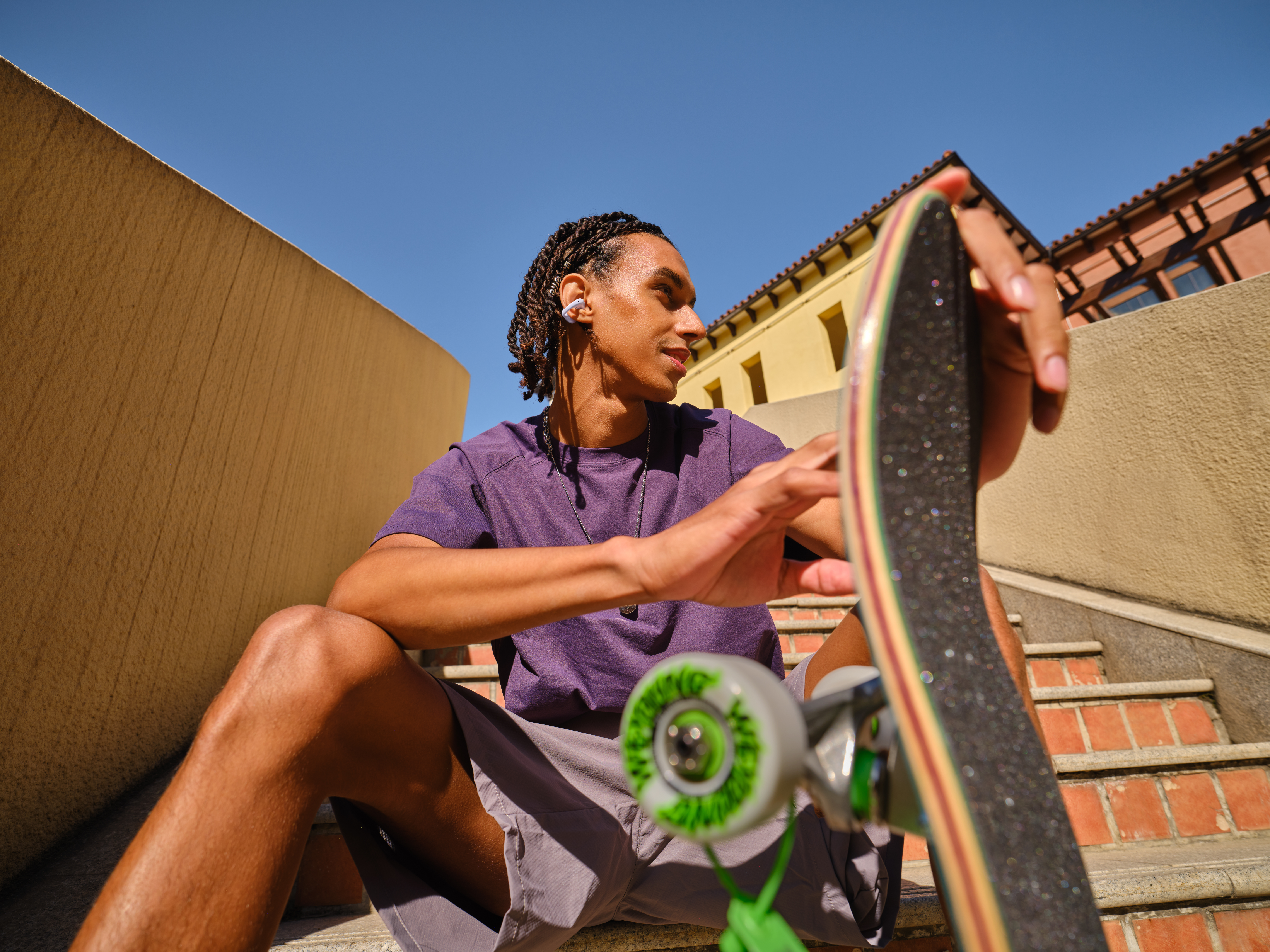 Ein Mann mit Zöpfen sitzt auf einer Treppe und hält ein Skateboard.