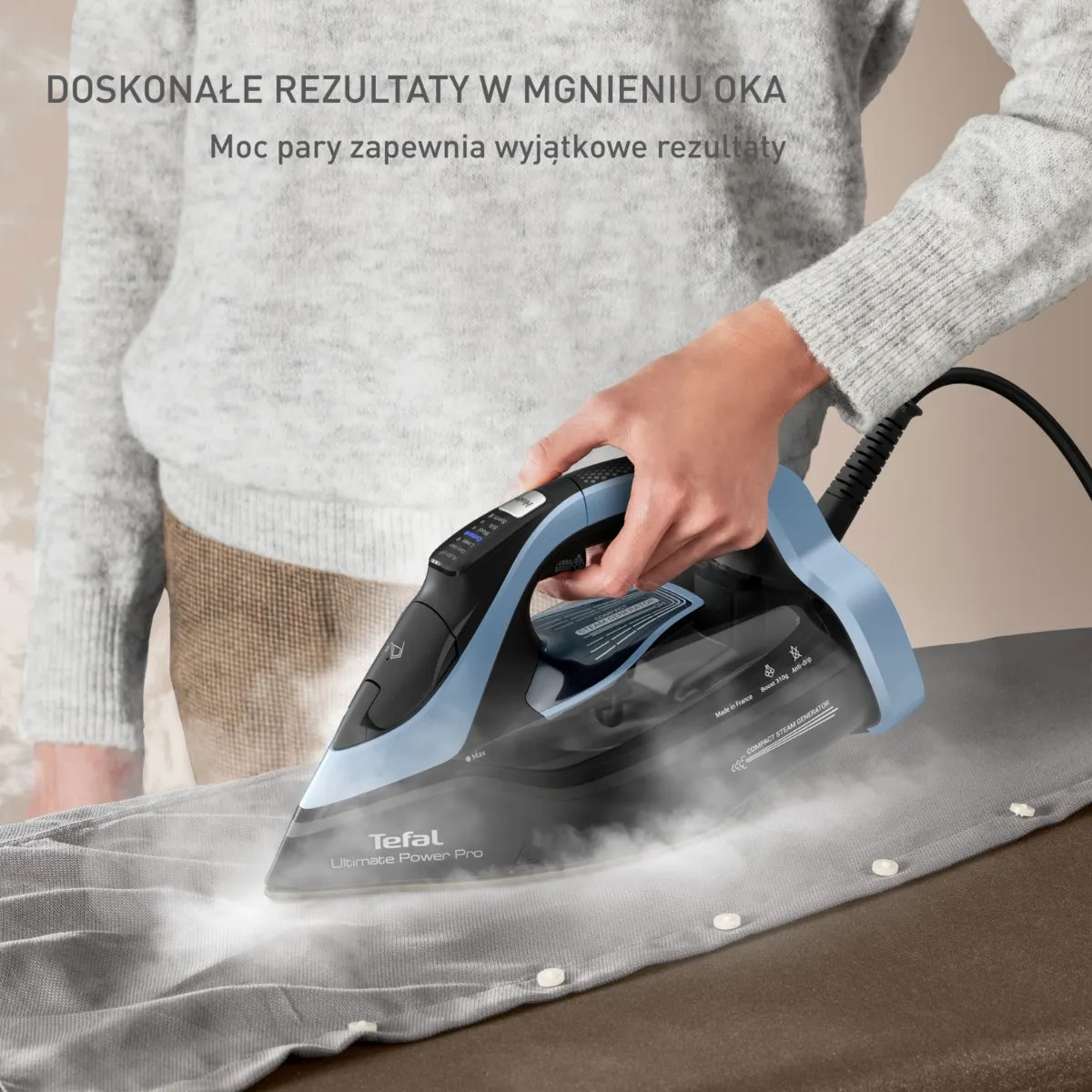 Ręka prasuje szarą koszulę niebieskim żelazkiem parowym Tefal.