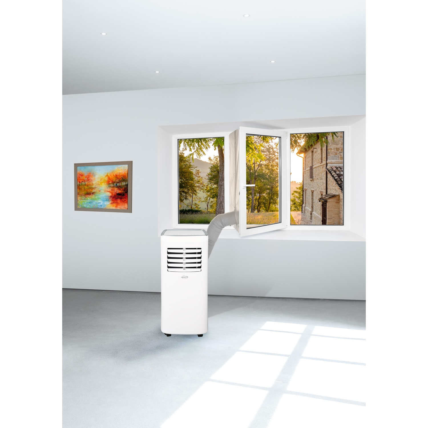 Un climatizzatore portatile bianco si trova in una stanza luminosa con un quadro e una finestra aperta.