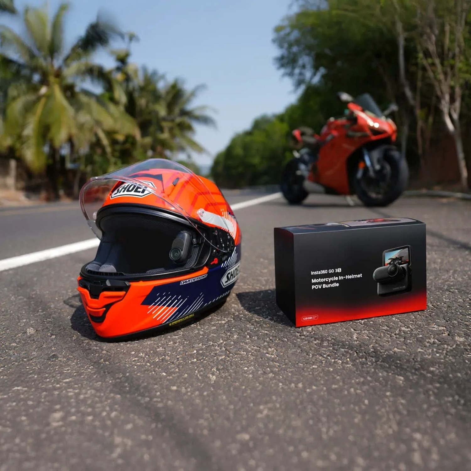 Un casco da moto arancione e una scatola per fotocamera appoggiati sull'asfalto.