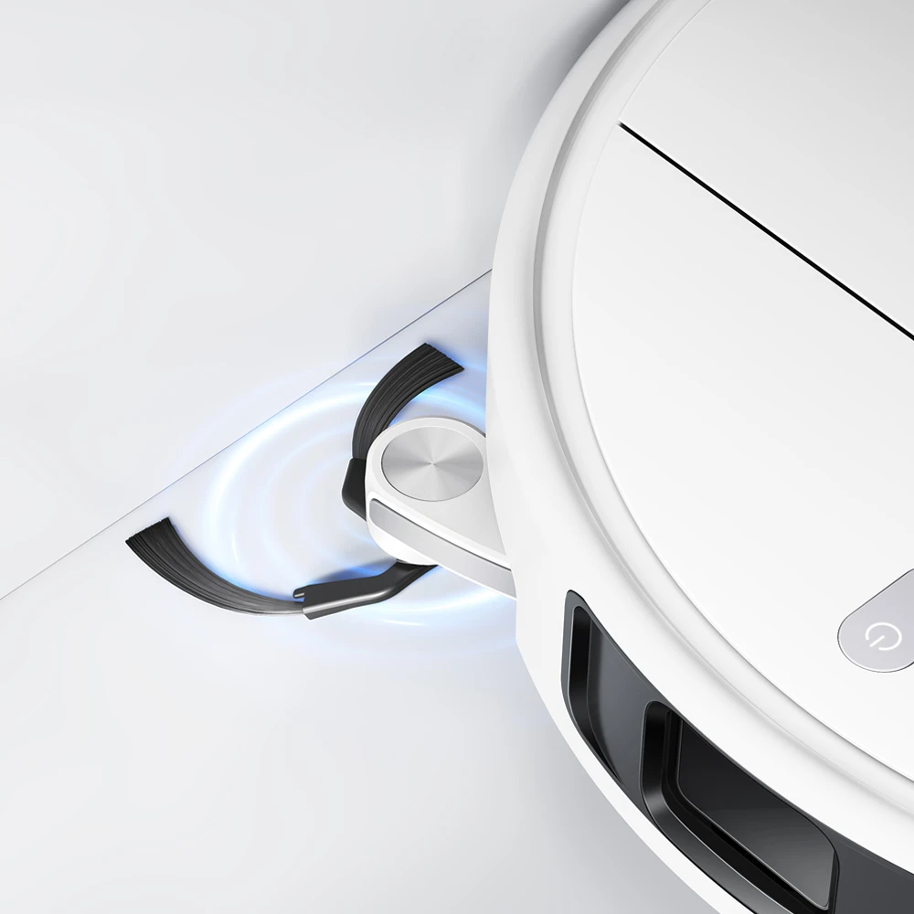 Un robot aspirateur blanc avec brosses latérales nettoie un coin blanc.