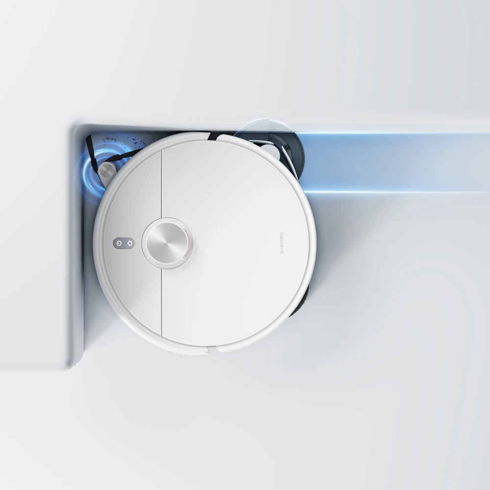 Un robot aspirateur blanc nettoie un coin, avec un faisceau lumineux bleu.