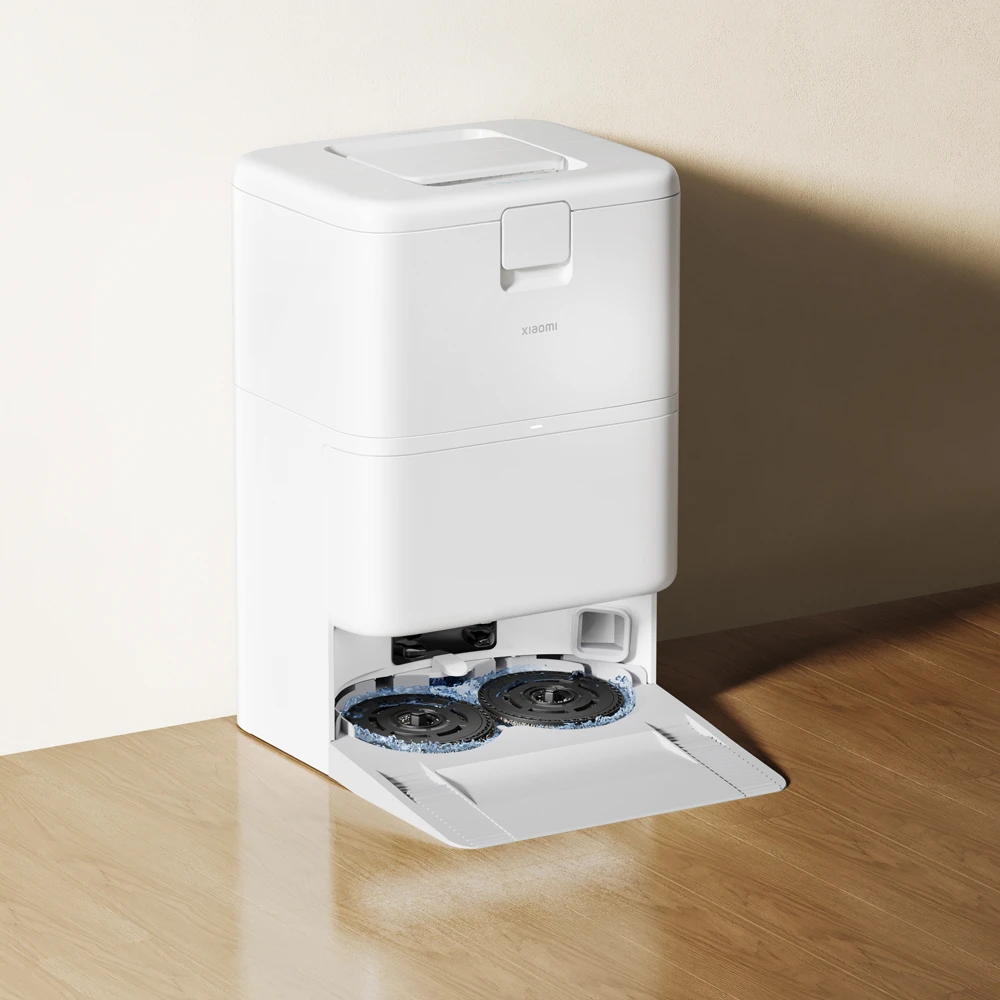 Un aspirateur robot blanc avec brosses rotatives sur un plancher en bois.