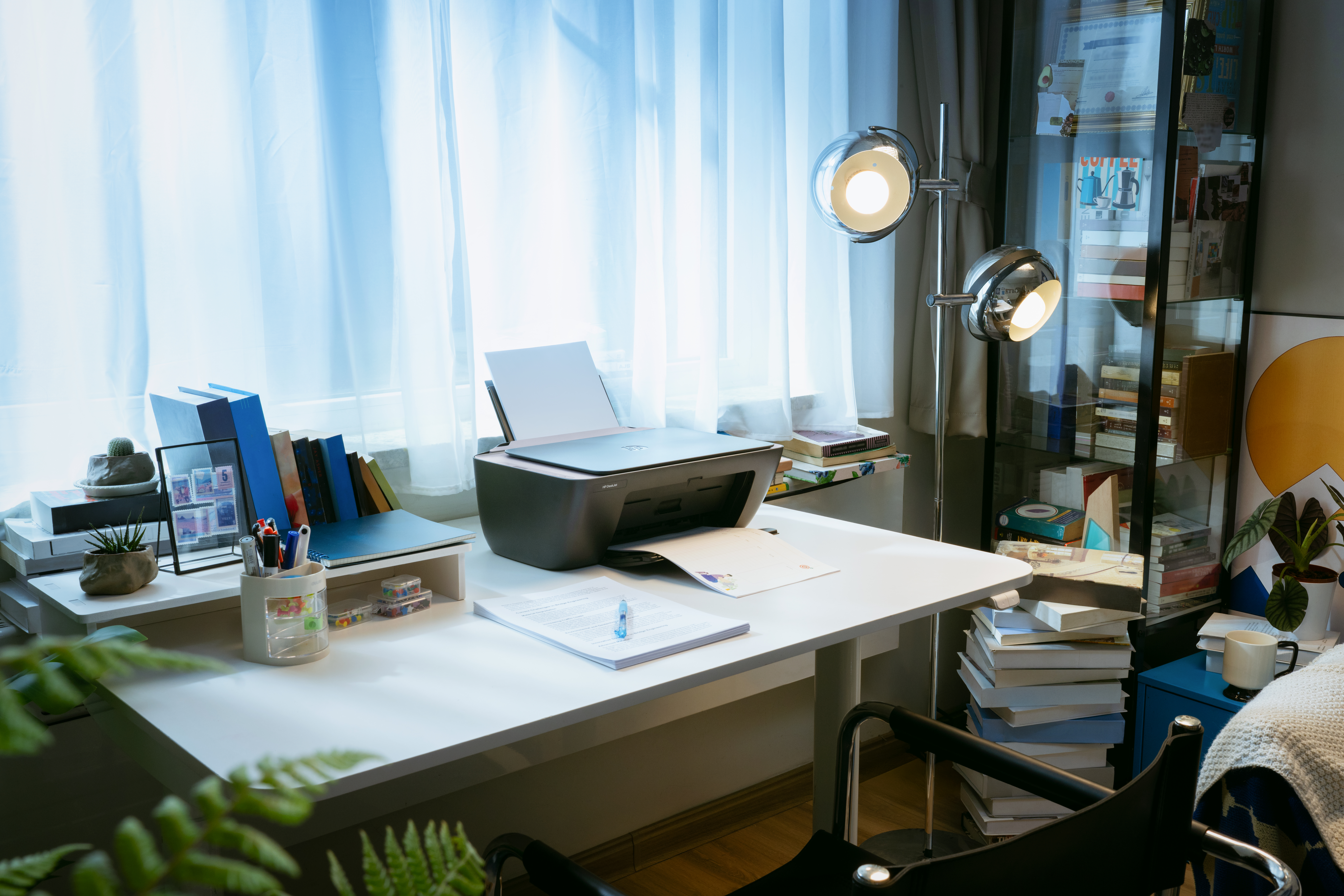 Ein Schreibtisch mit Drucker, Büchern und Pflanzen im Büro.