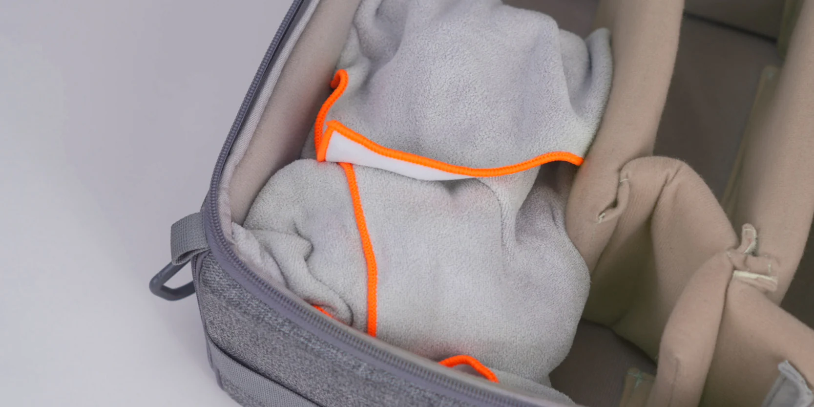 Graue Tasche mit orangefarbenen Nähten und einem gefalteten grauen Tuch.