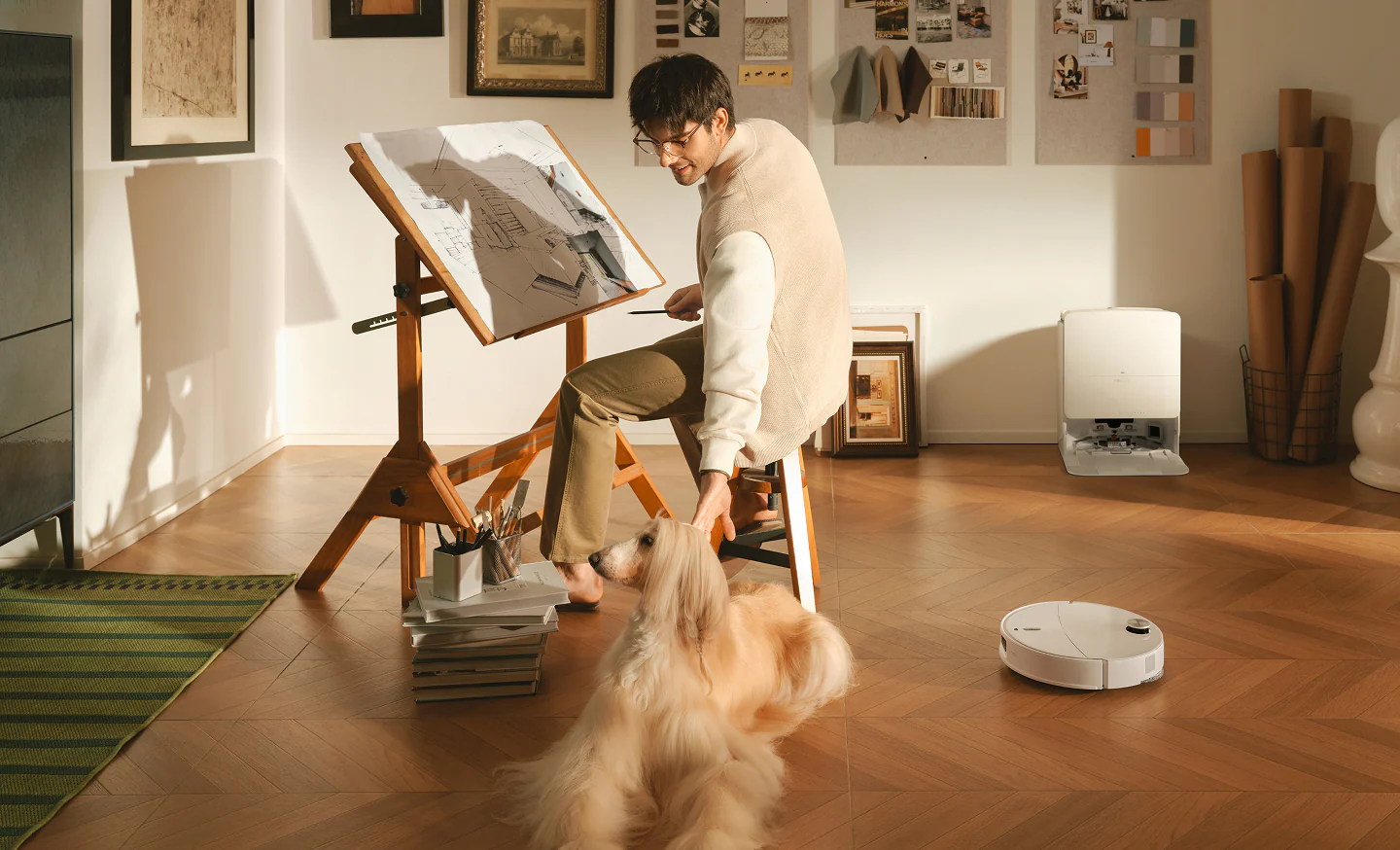 Uomo con cane a tavolo da disegno, robot aspirapolvere pulisce pavimento.