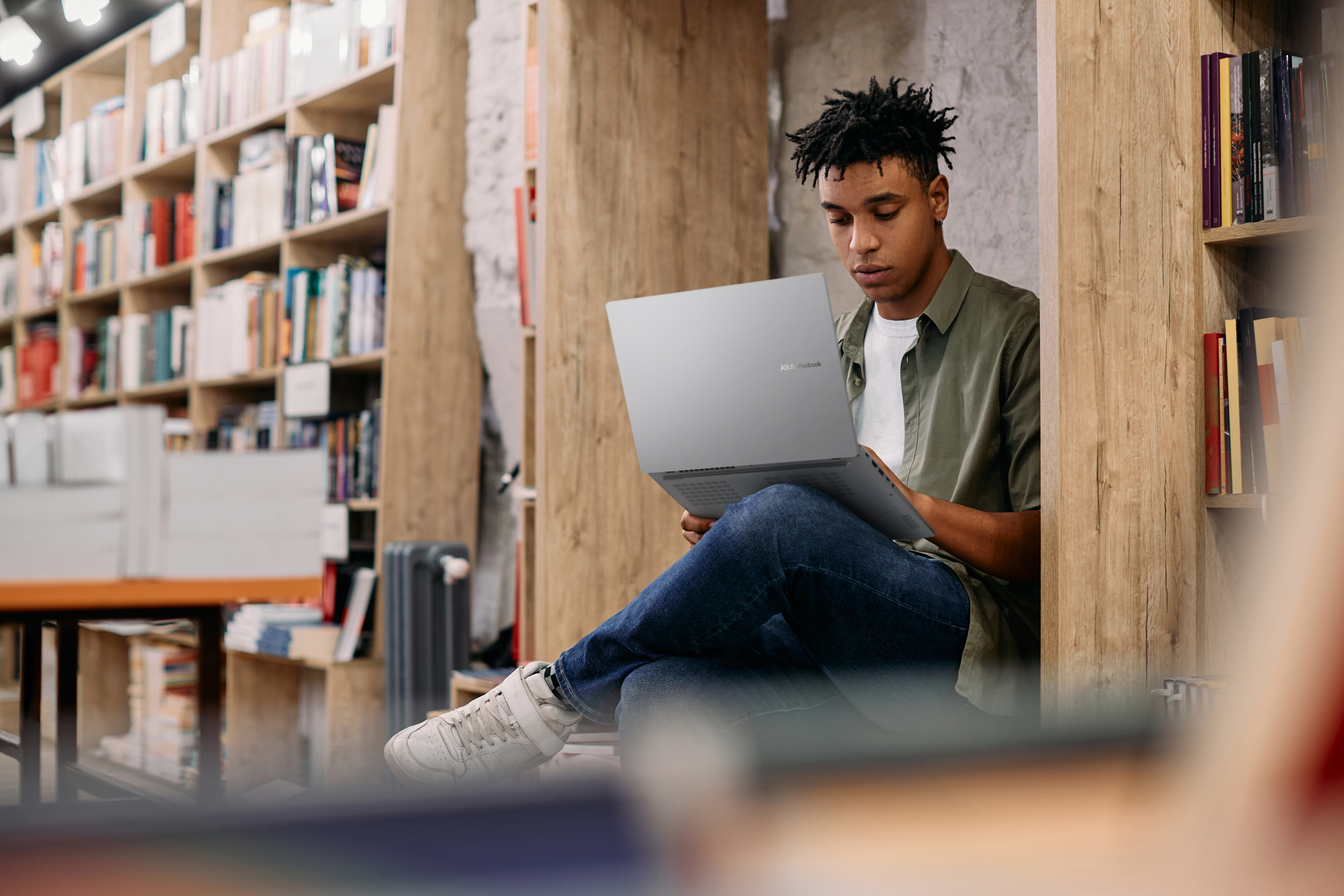 Een man zit in een boekenrek en gebruikt een laptop.