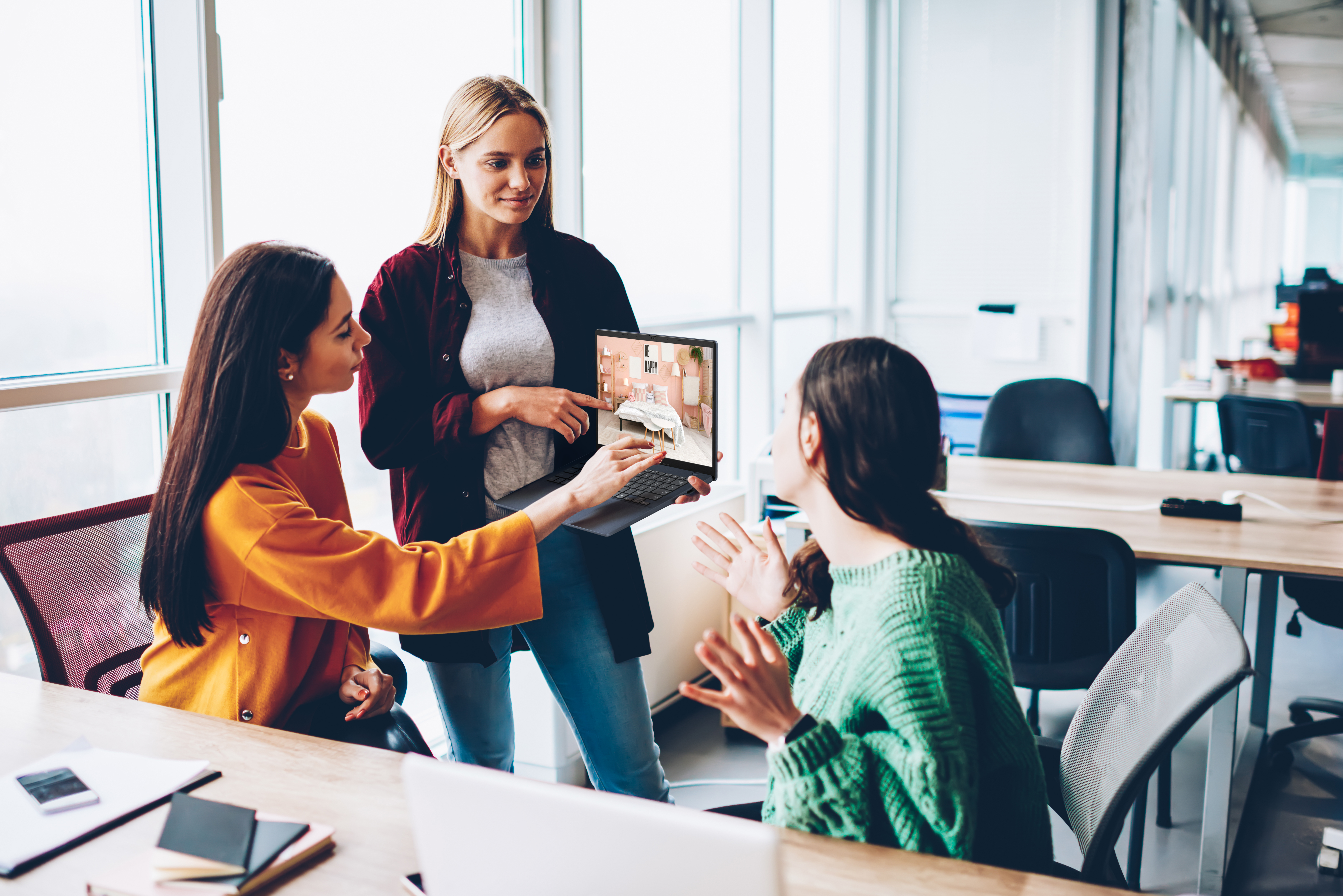 Drie vrouwen bespreken een laptopscherm met een slaapkamerinterieur.