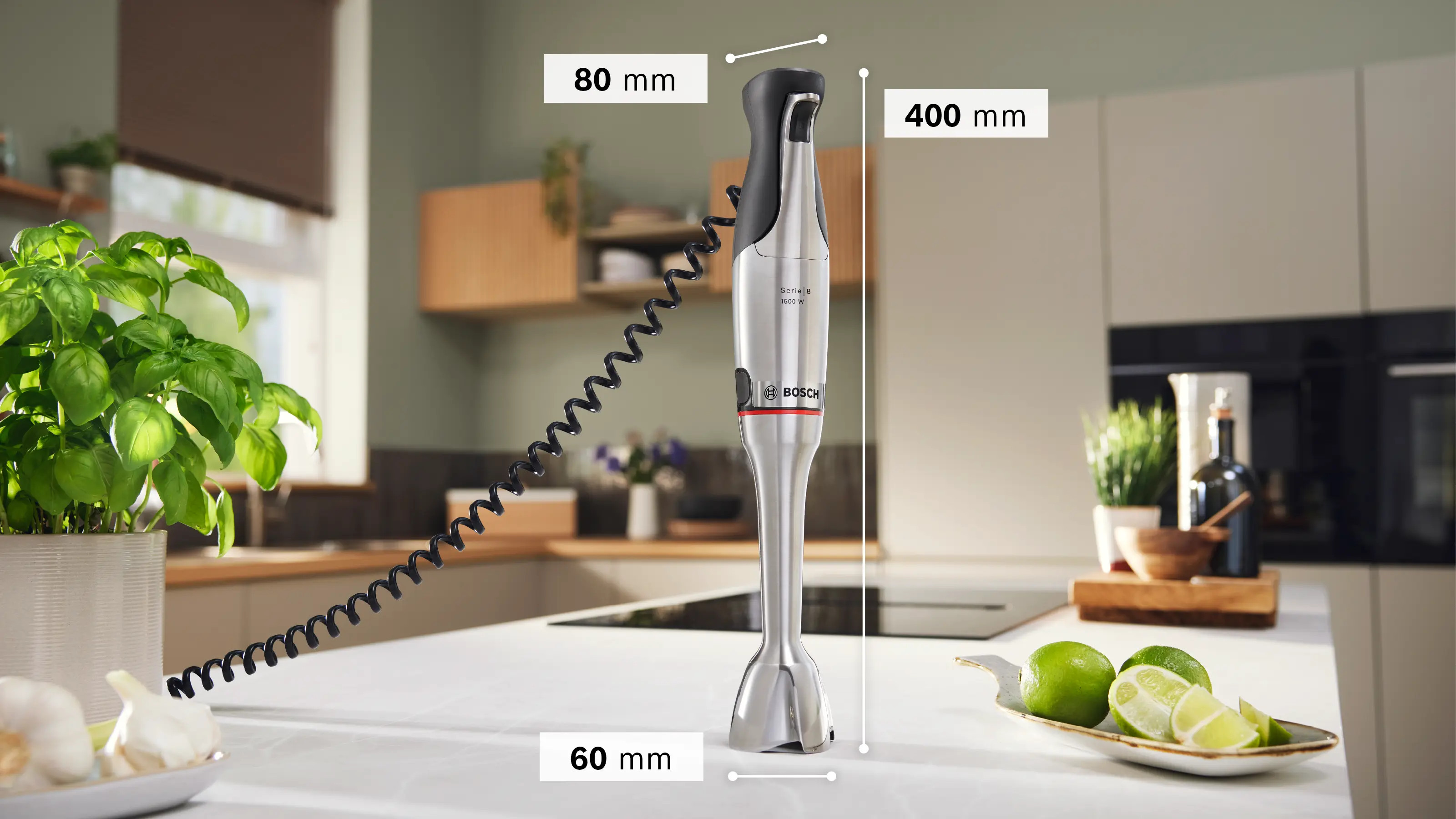 Srebrny blender ręczny z czarnym uchwytem stoi na blacie. Obok leżą limonki.