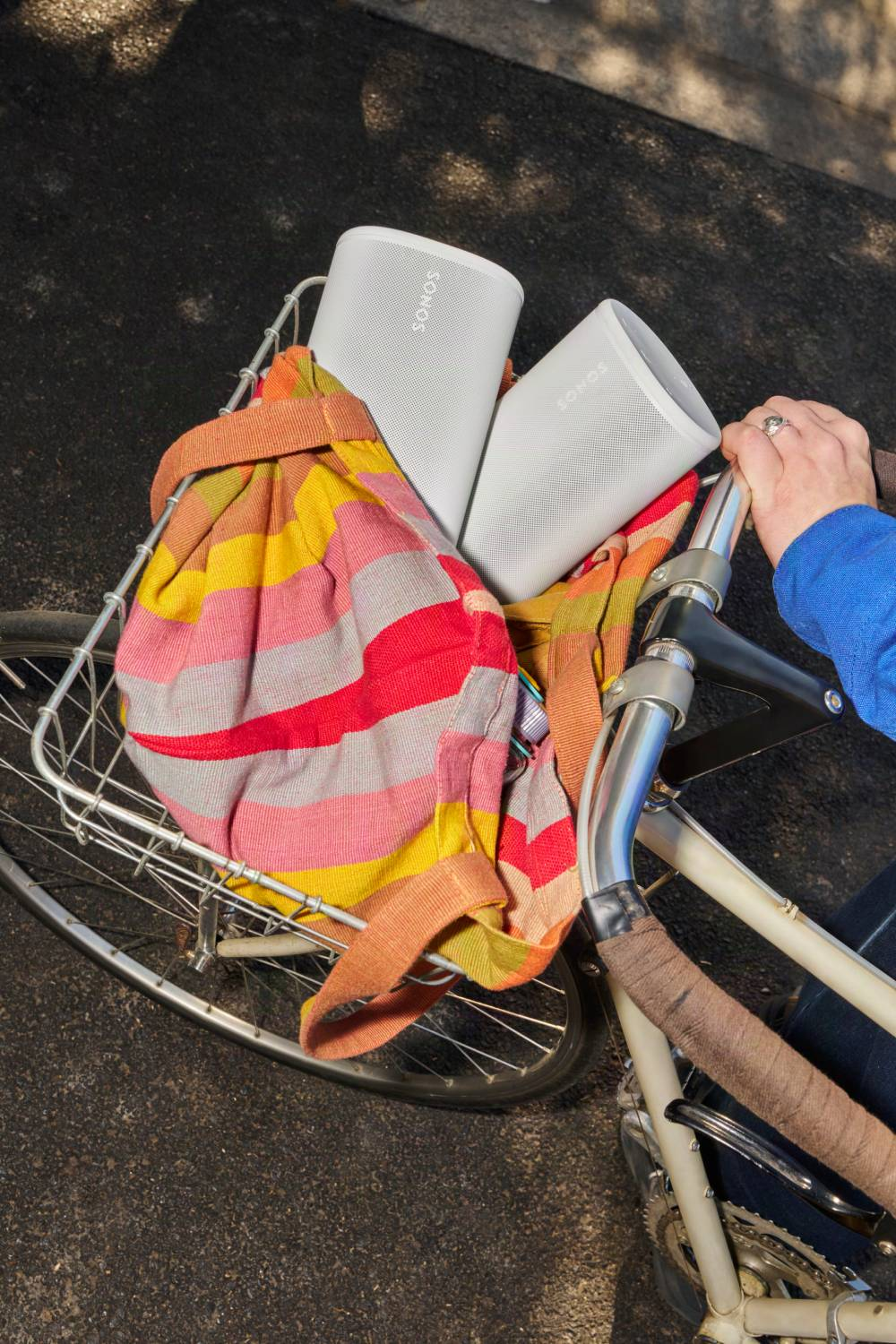 Dos altavoces Sonos blancos en la cesta de una bicicleta con bolsa colorida.