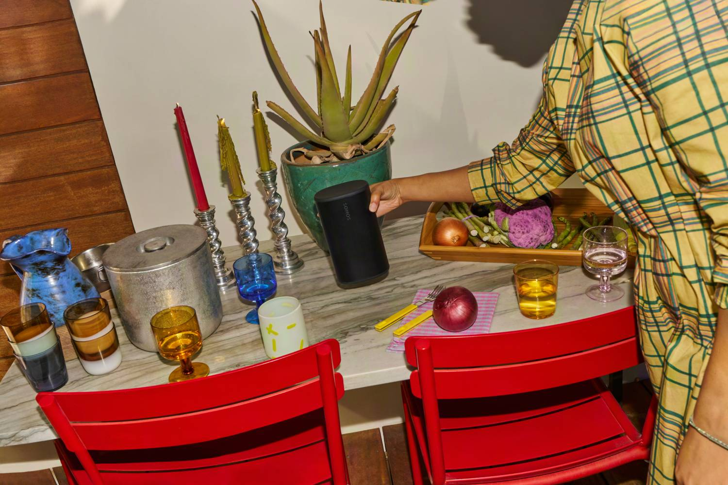 Sillas rojas en mesa de mármol con comida, bebidas y altavoz.