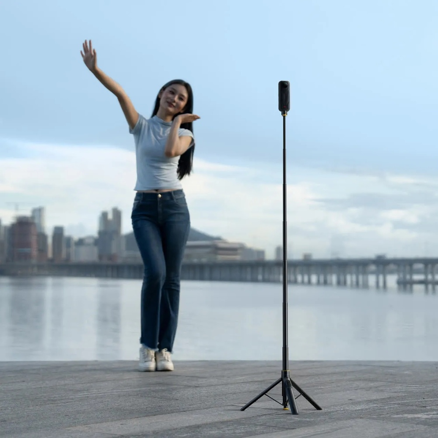 Una donna saluta davanti a un treppiede per fotocamera a 360 gradi sull'acqua.