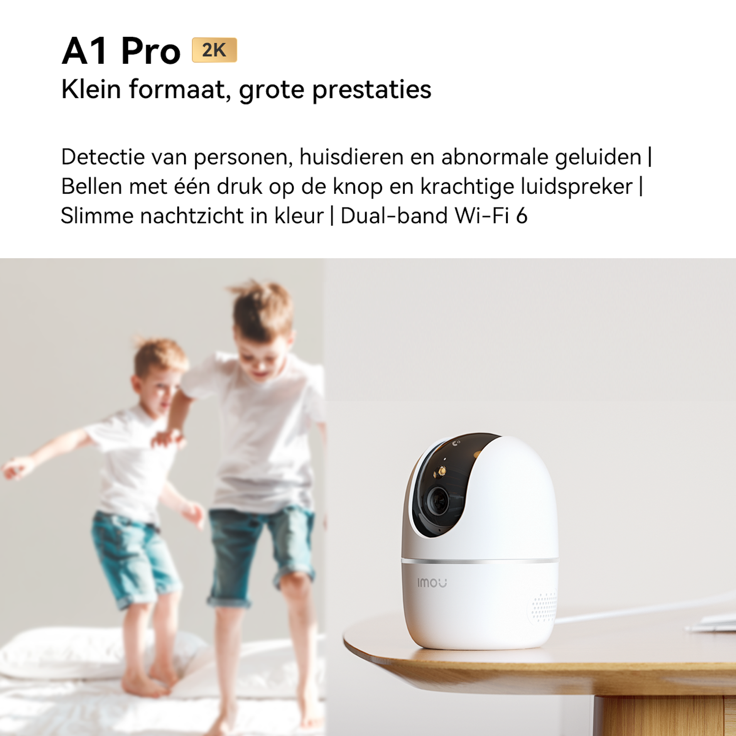A white security camera sits on a wooden table, two boys jump on a bed behind it.