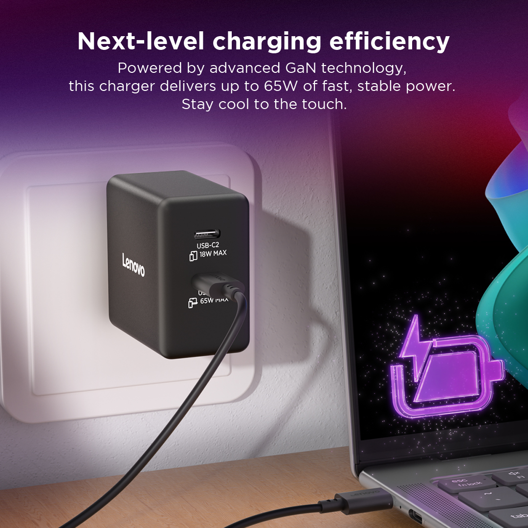 Un cargador Lenovo negro de 65W alimenta un portátil, enchufado a la pared.
