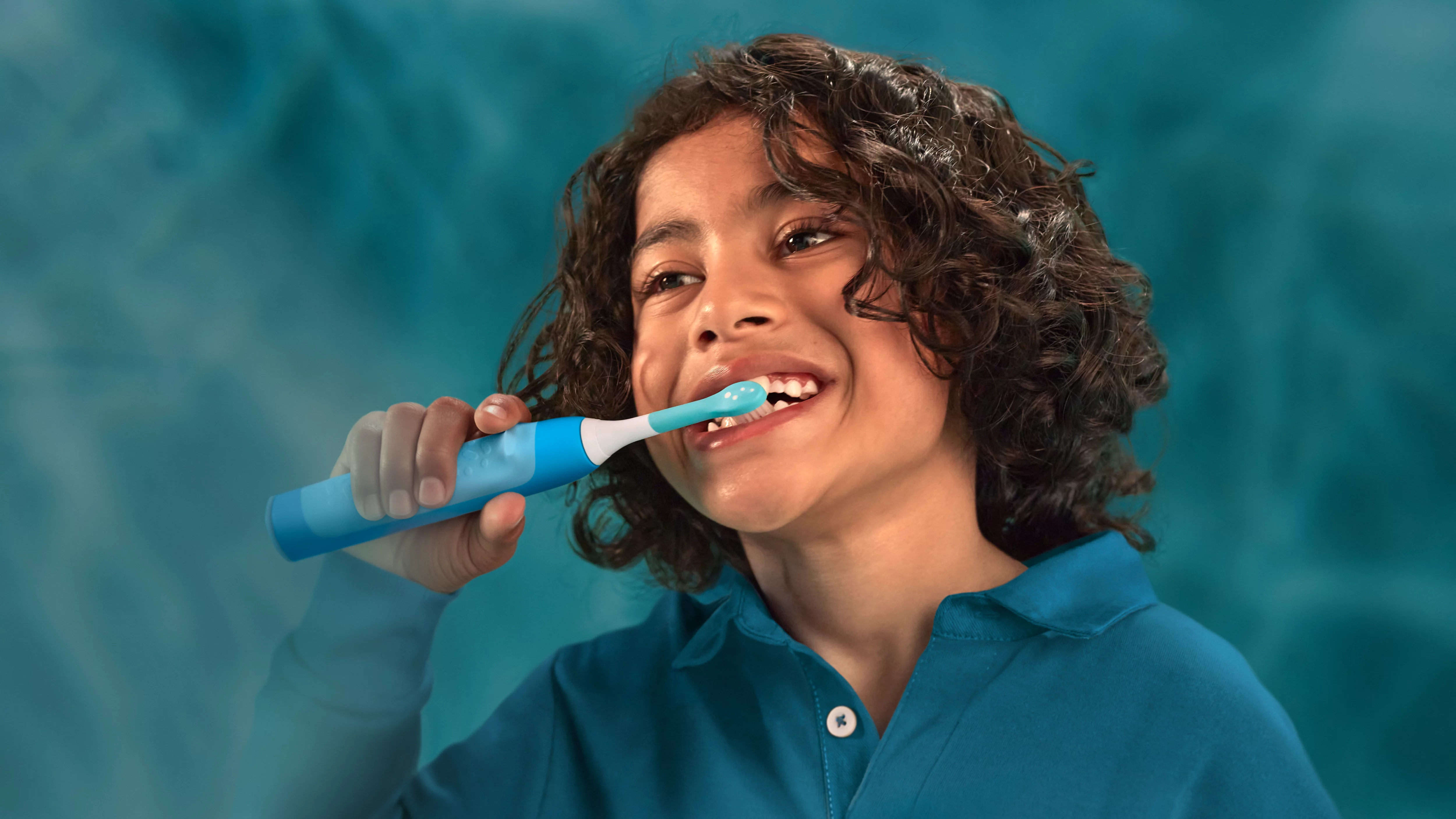 Un ragazzo si lava i denti con uno spazzolino elettrico blu.