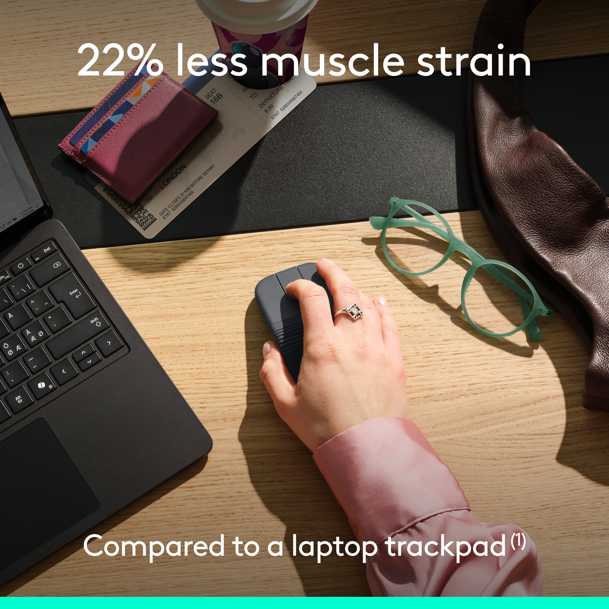 Una mano usa un mouse grigio su una scrivania di legno con laptop, occhiali e borsa.