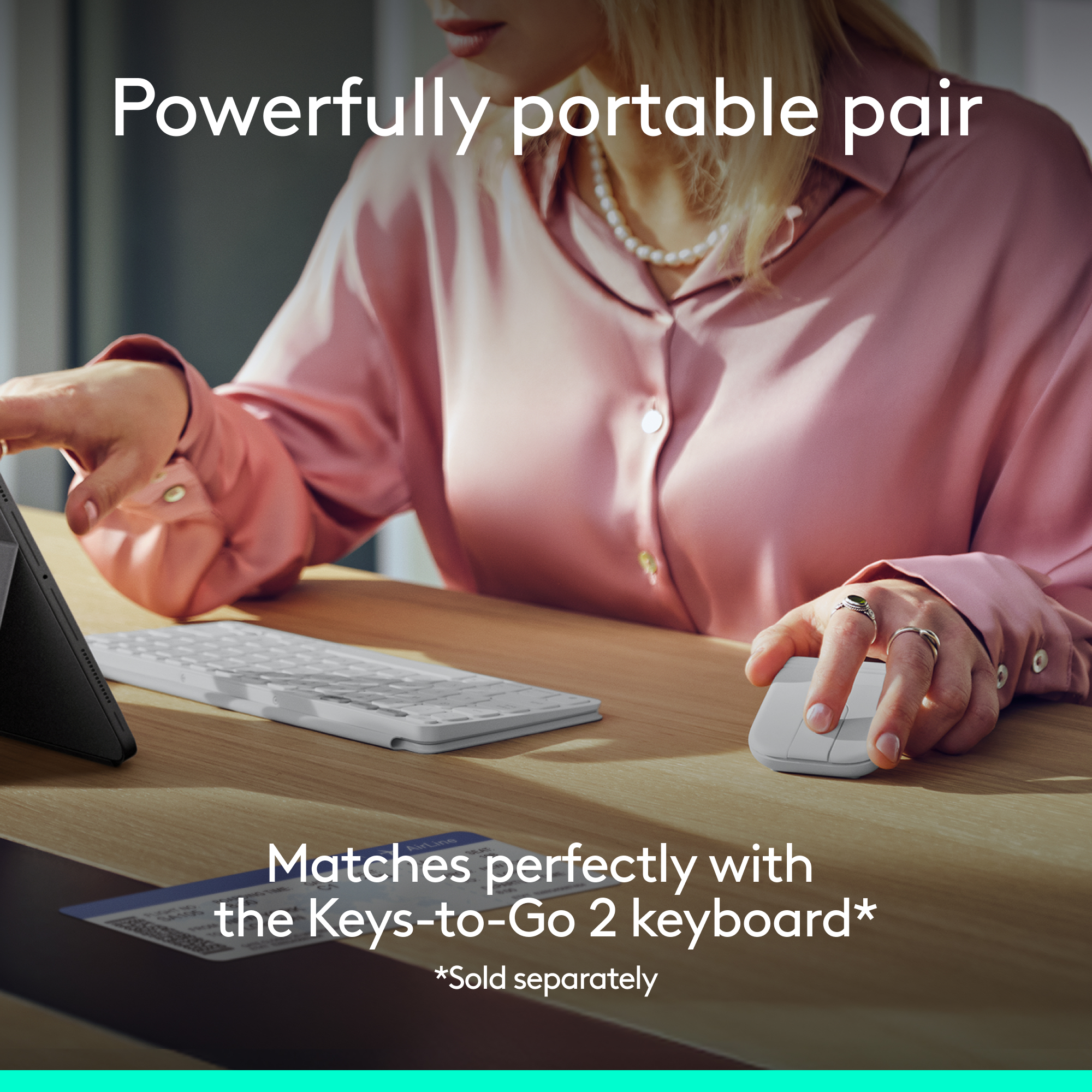 Una persona usa un mouse e una tastiera bianchi con un tablet su una scrivania di legno.