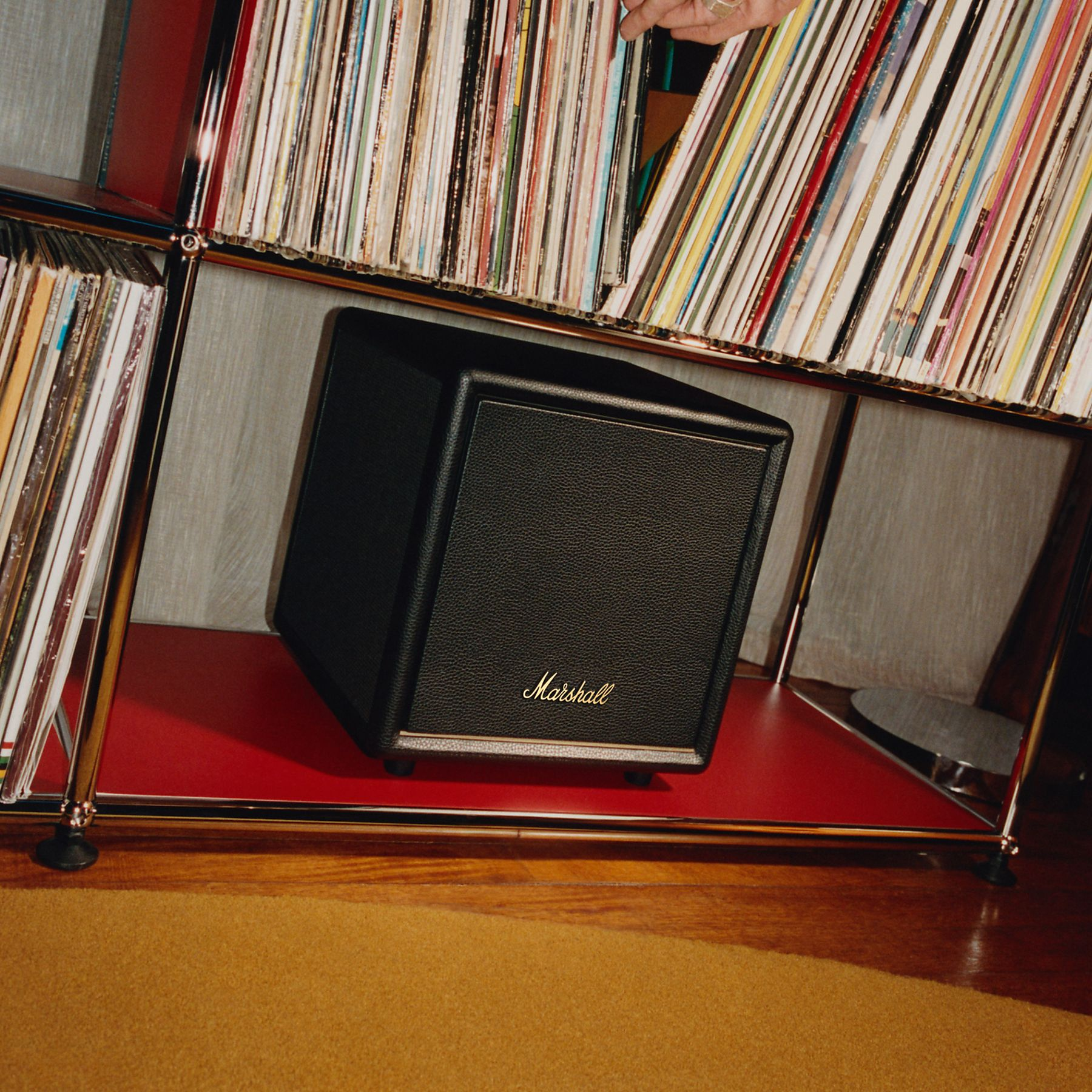 Un altavoz Marshall negro se asienta en un estante rojo junto a discos de vinilo.