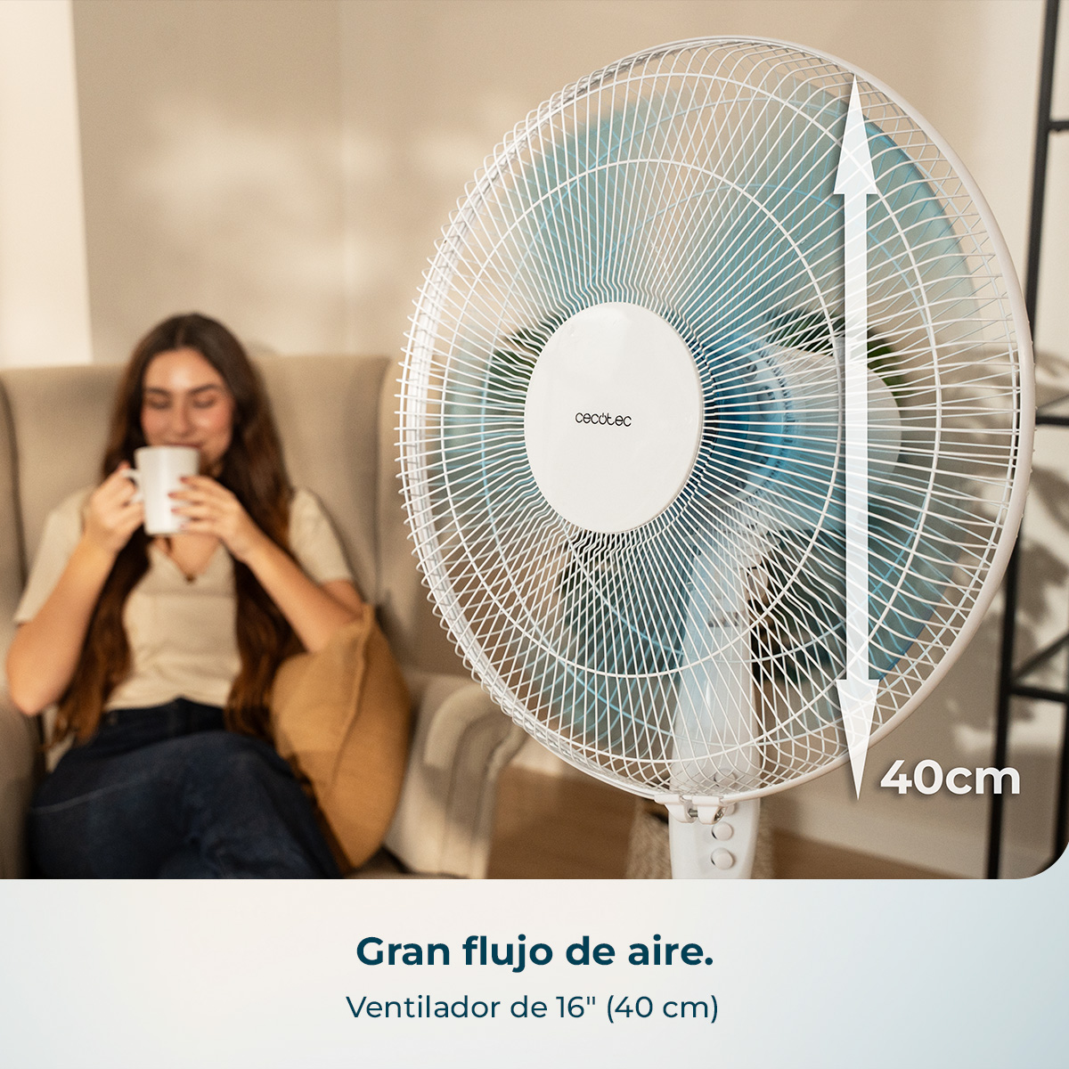 Un ventilador de pie blanco de 40cm está frente a una mujer sentada en un sofá.