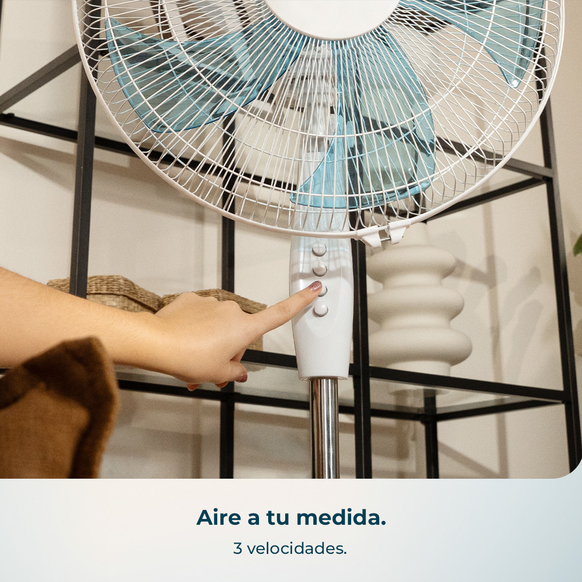 Una mano presiona los botones de un ventilador de pie blanco con aspas azules.