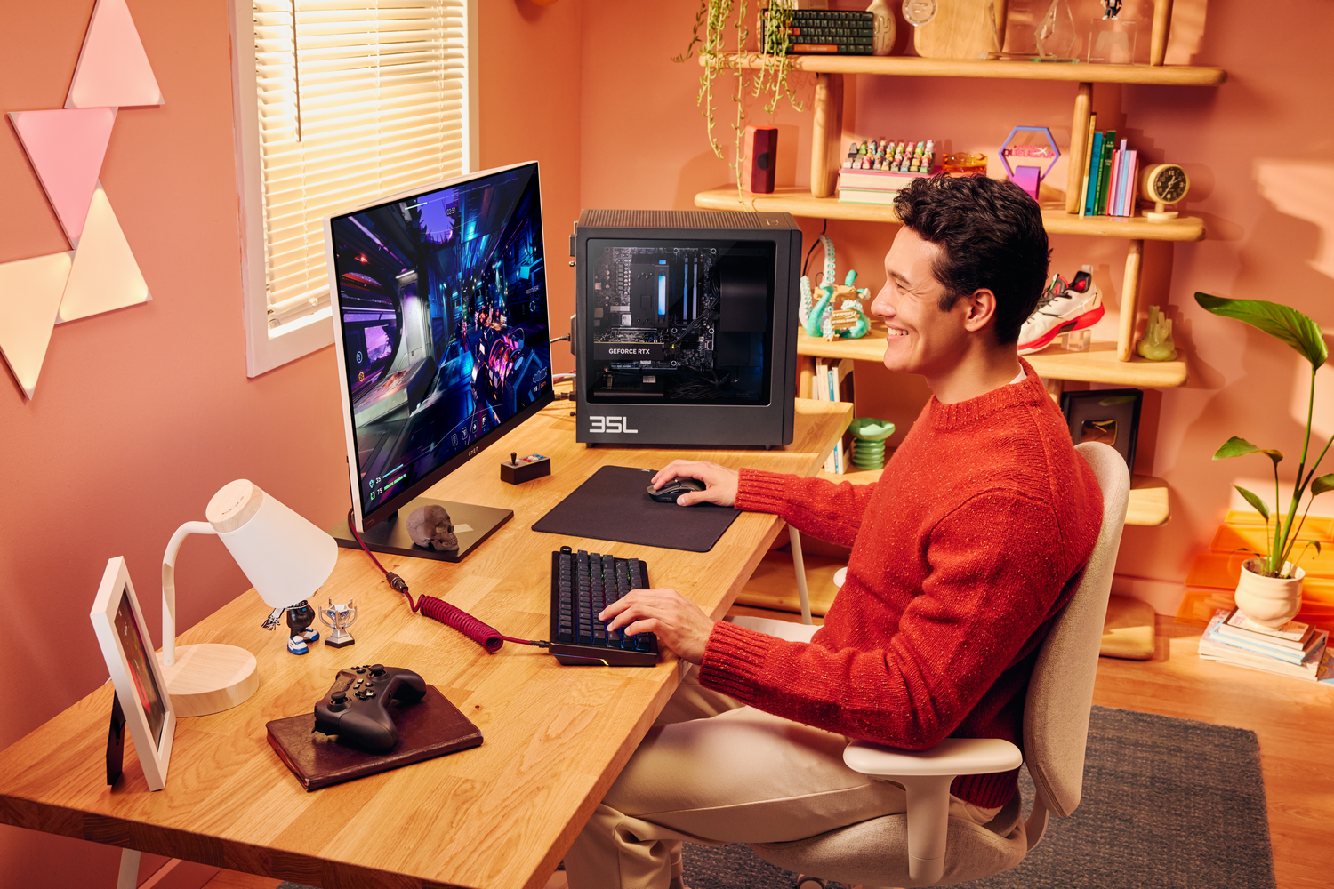 Un hombre con suéter rojo juega en una computadora en una habitación naranja.