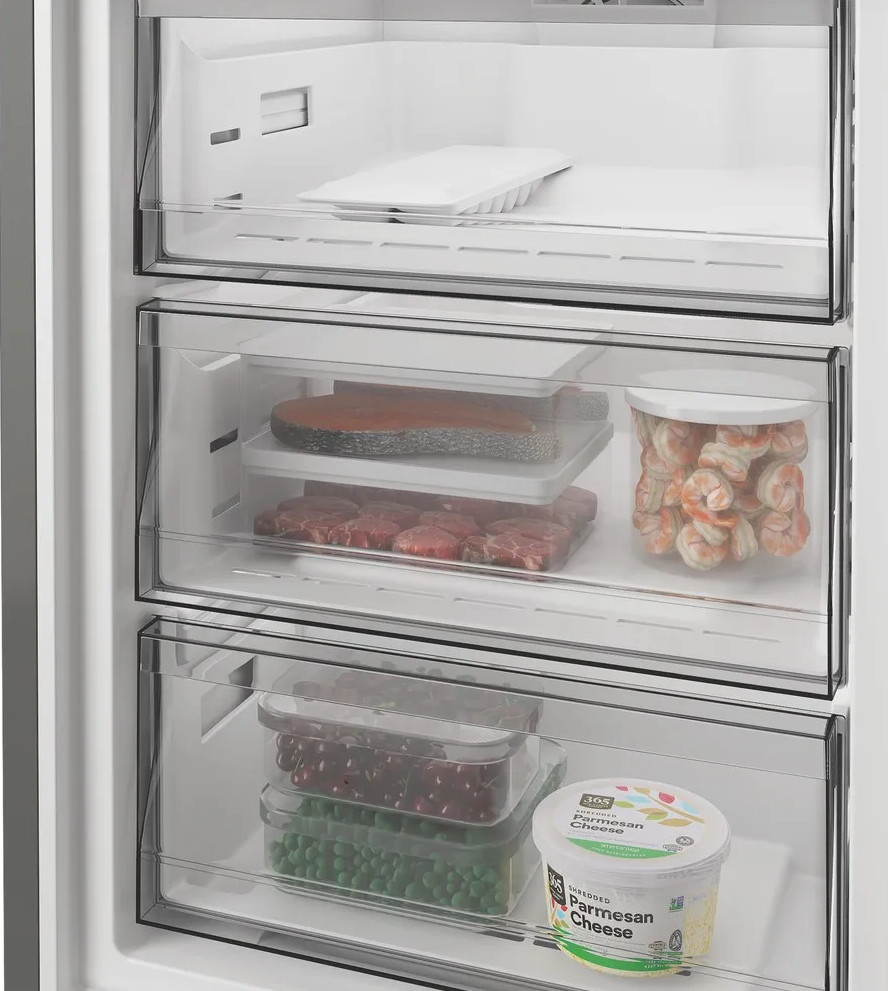 Otwarte szuflady zamrażarki: tacka na lód, łosoś, steki, krewetki, jagody, groszek, ser.