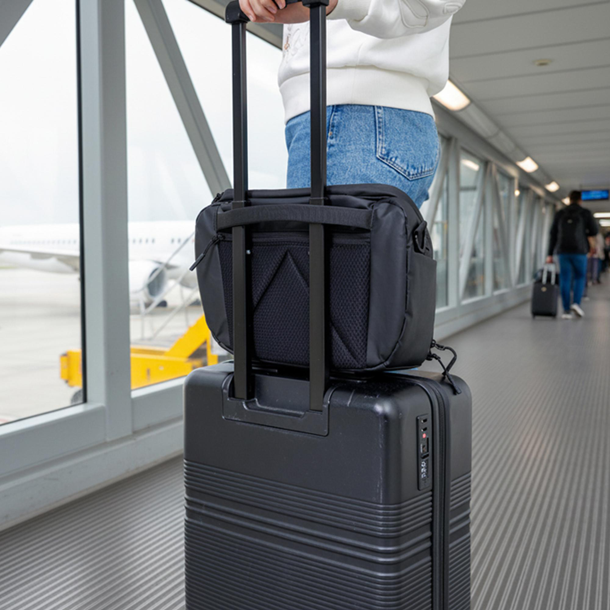 Person in Jeans und weißem Hoodie am Flughafentor mit schwarzem Gepäck. Flugzeug sichtbar.
