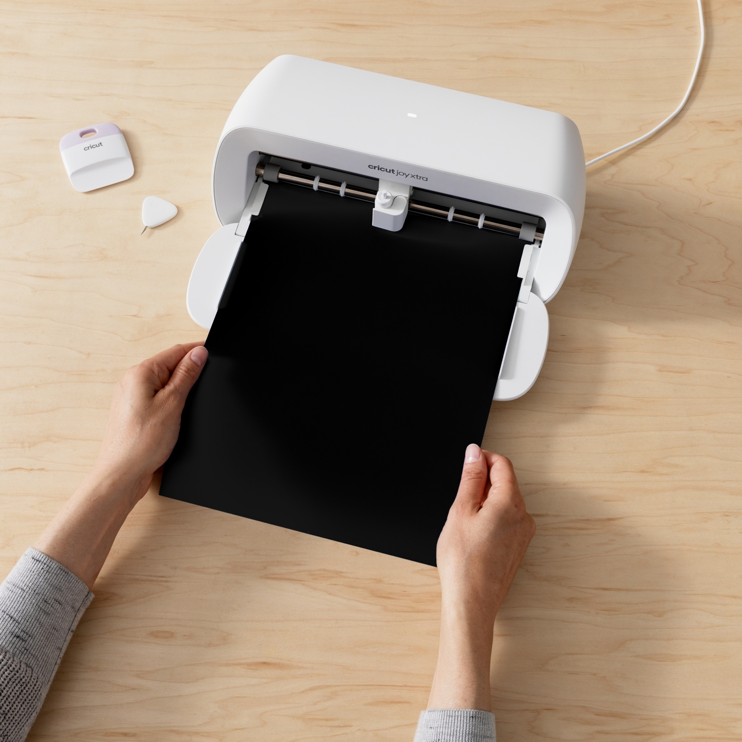 Mani inseriscono carta nera in taglierina Cricut Joy Xtra bianca su tavolo legno.
