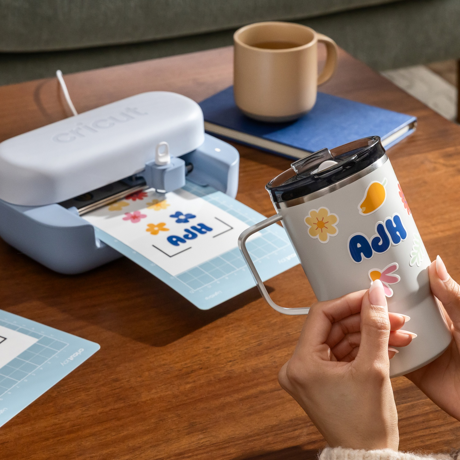 Una persona applica adesivi su una tazza mentre una macchina Cricut stampa.