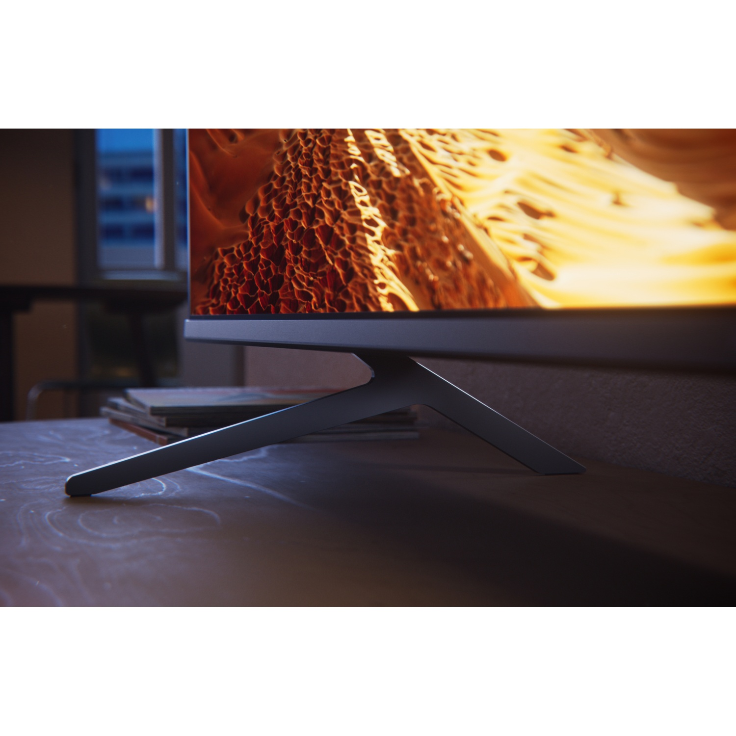 A modern TV displaying an abstract orange image sits on a wooden table.