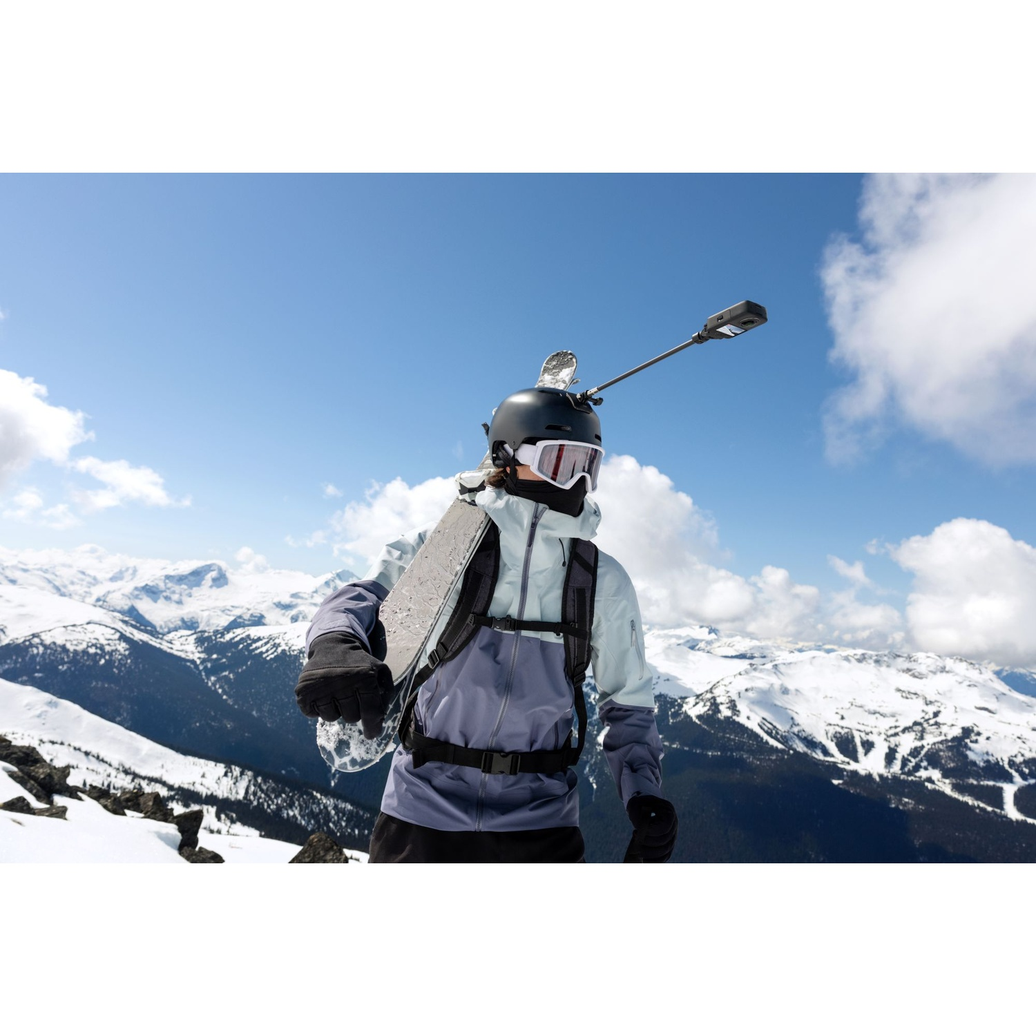 Uno snowboarder con casco e fotocamera, con montagne innevate sullo sfondo.