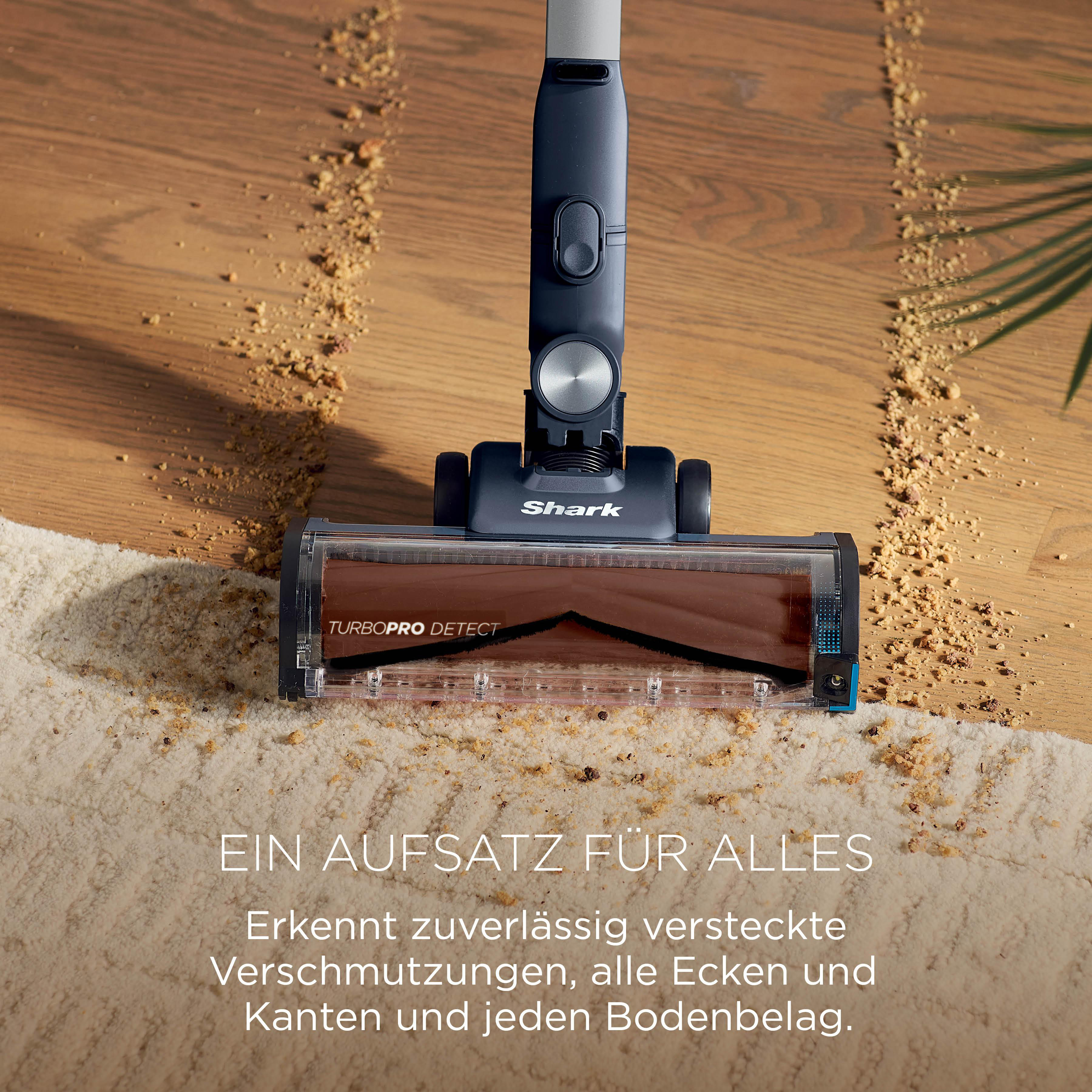 Ein Shark Staubsaugeraufsatz reinigt Teppich und Holz. Krümel liegen auf dem Boden.