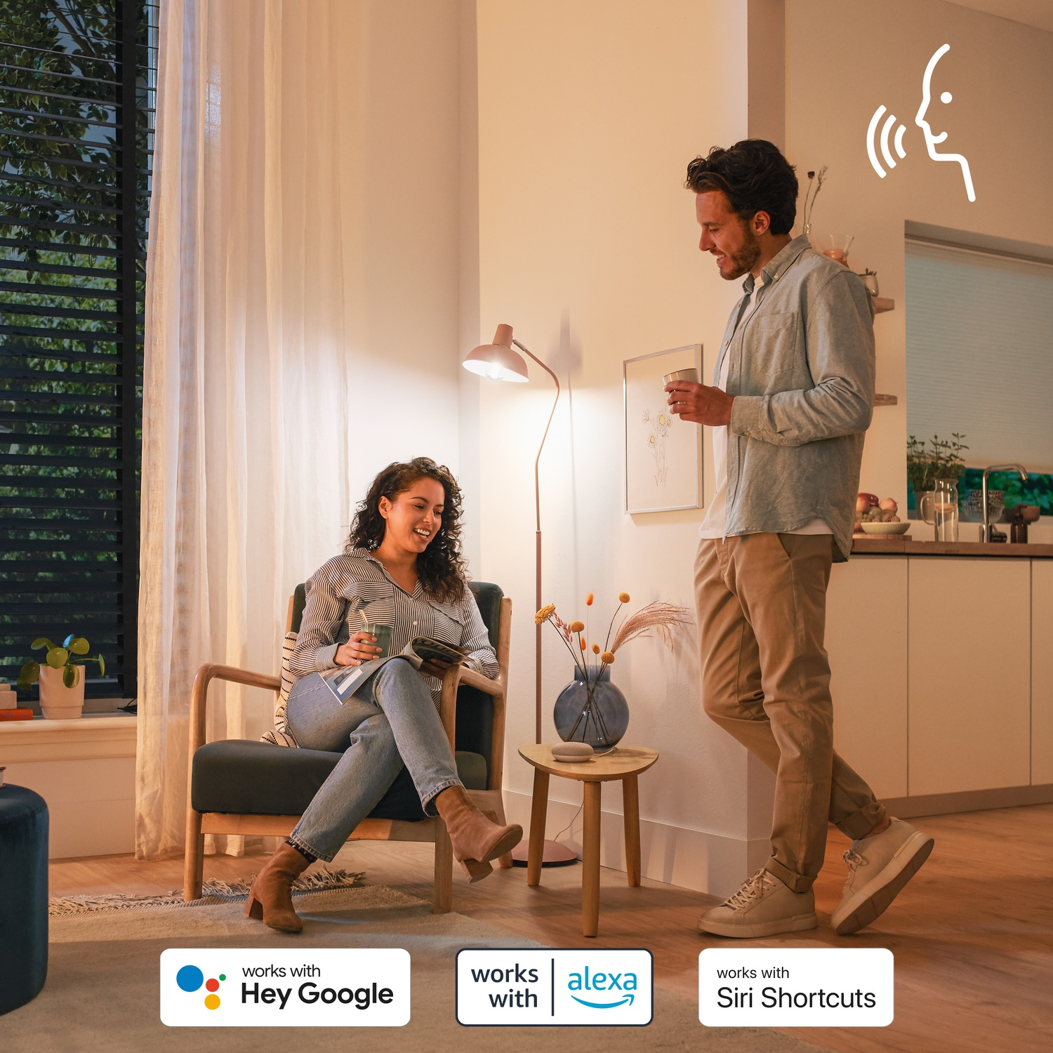 Homme et femme dans un salon, près de logos d'assistants vocaux.