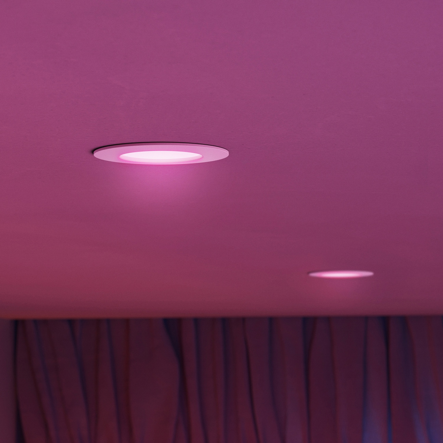 Deux spots encastrés éclairent un plafond rose. Des rideaux violets sont visibles en dessous.
