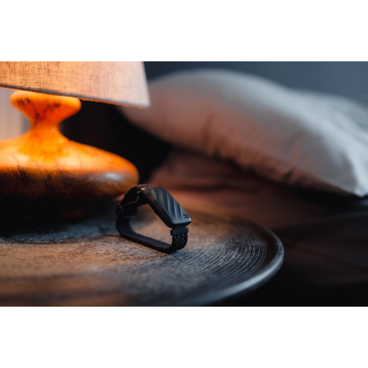 Een zwarte fitnesstracker ligt op een donkere houten tafel naast een lamp.